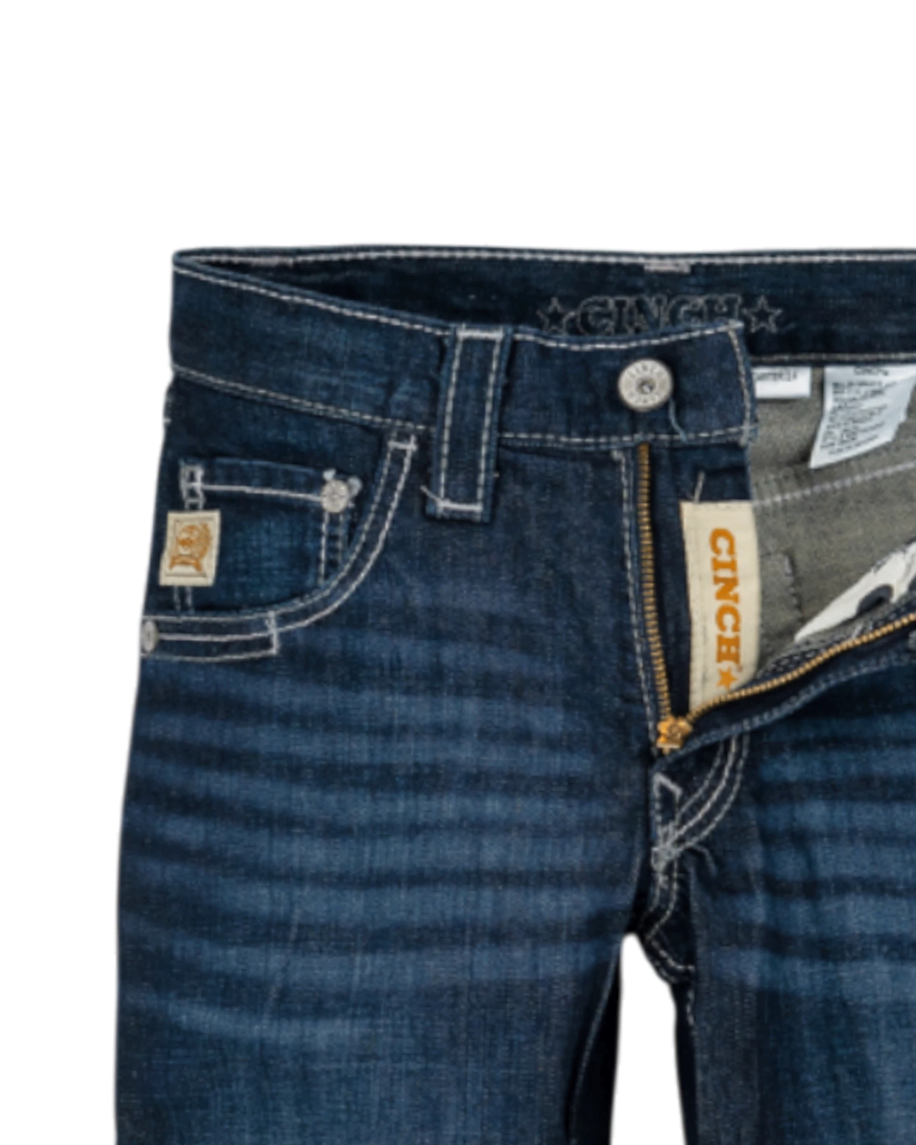 Close-up of the front of dark blue denim jeans with light fading, featuring a coin pocket with a small embroidered patch, belt loops, and a button closure with a zipper fly. The waistband has 'CINCH' stitched on it