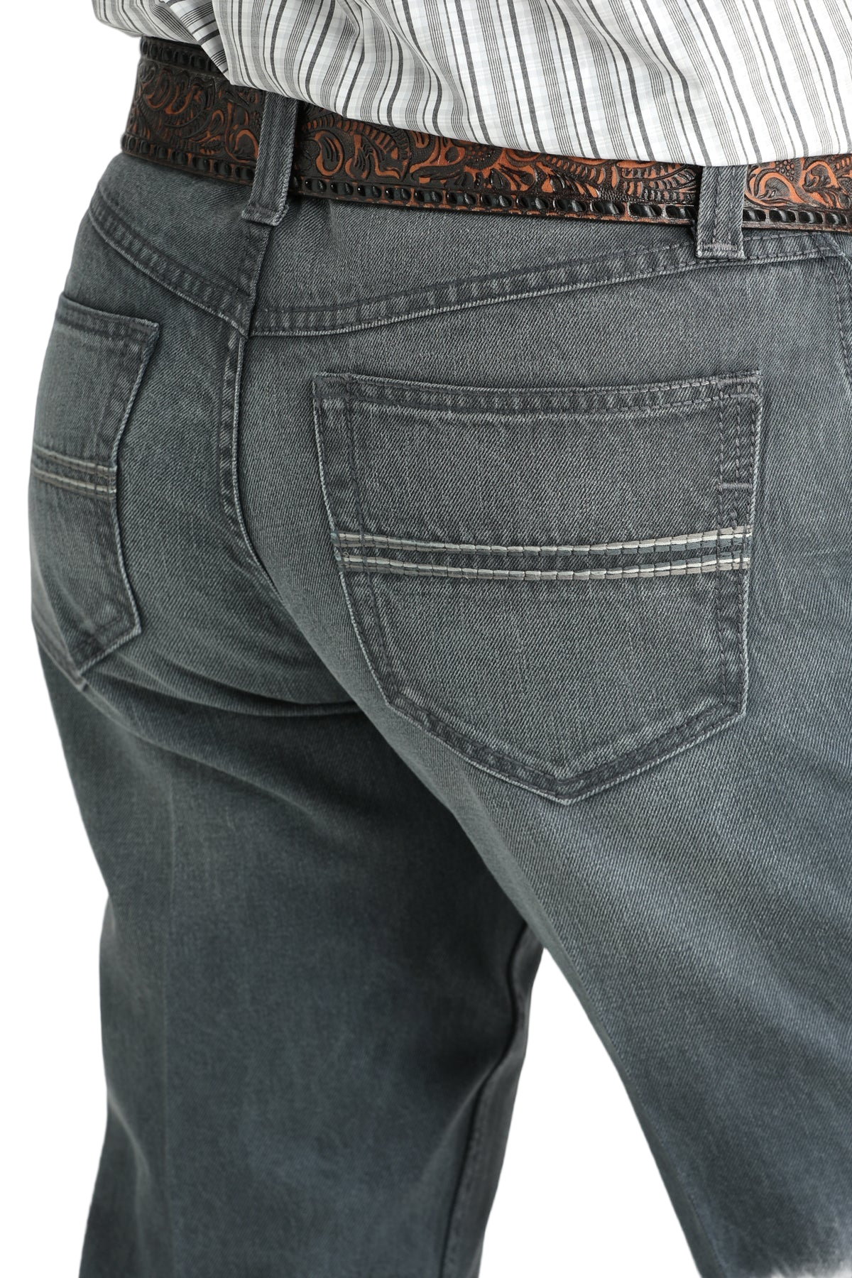 Close-up of the back of a person wearing gray denim jeans with simple stitching on the back pockets and a tooled brown leather belt, paired with a tucked-in patterned shirt