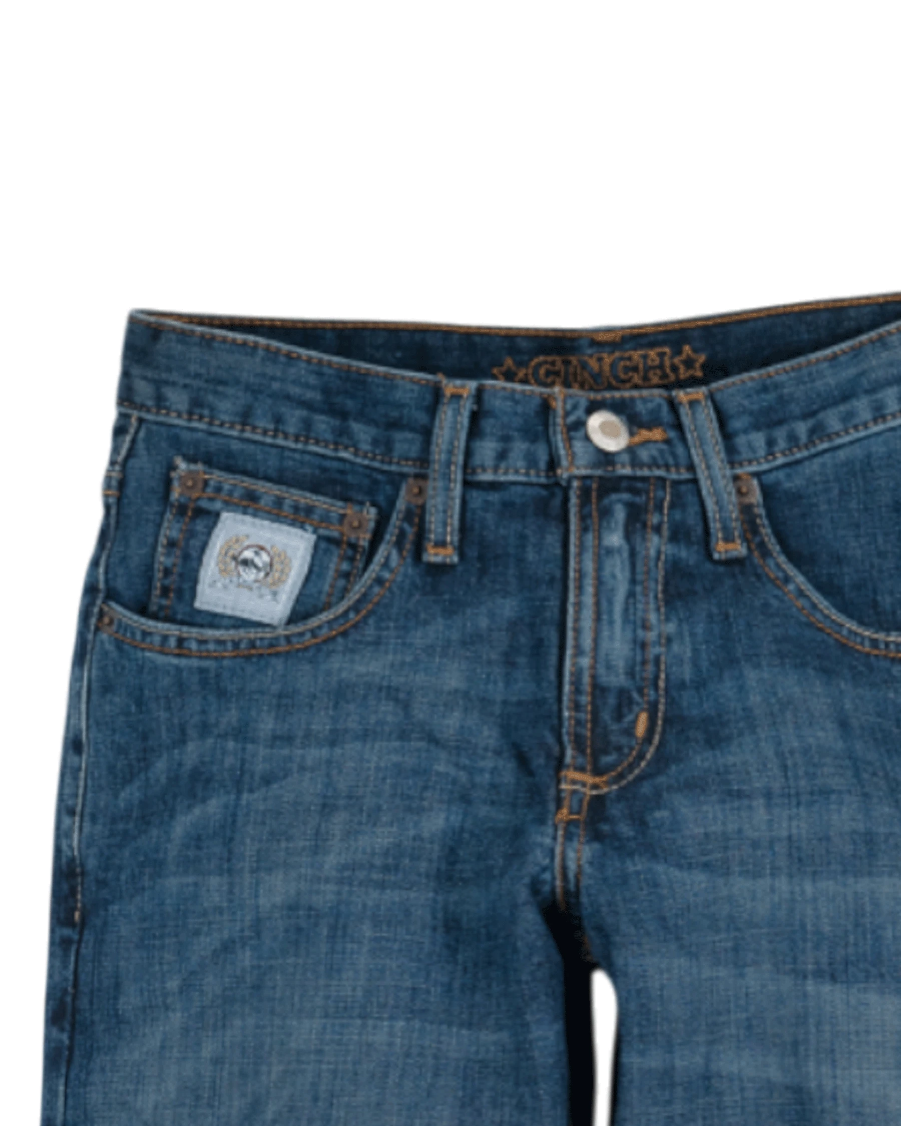 Close-up of the front of blue denim jeans with light fading, featuring a coin pocket with a small embroidered patch, belt loops, and a button closure with a zipper fly. The waistband has 'CINCH' stitched in gold thread