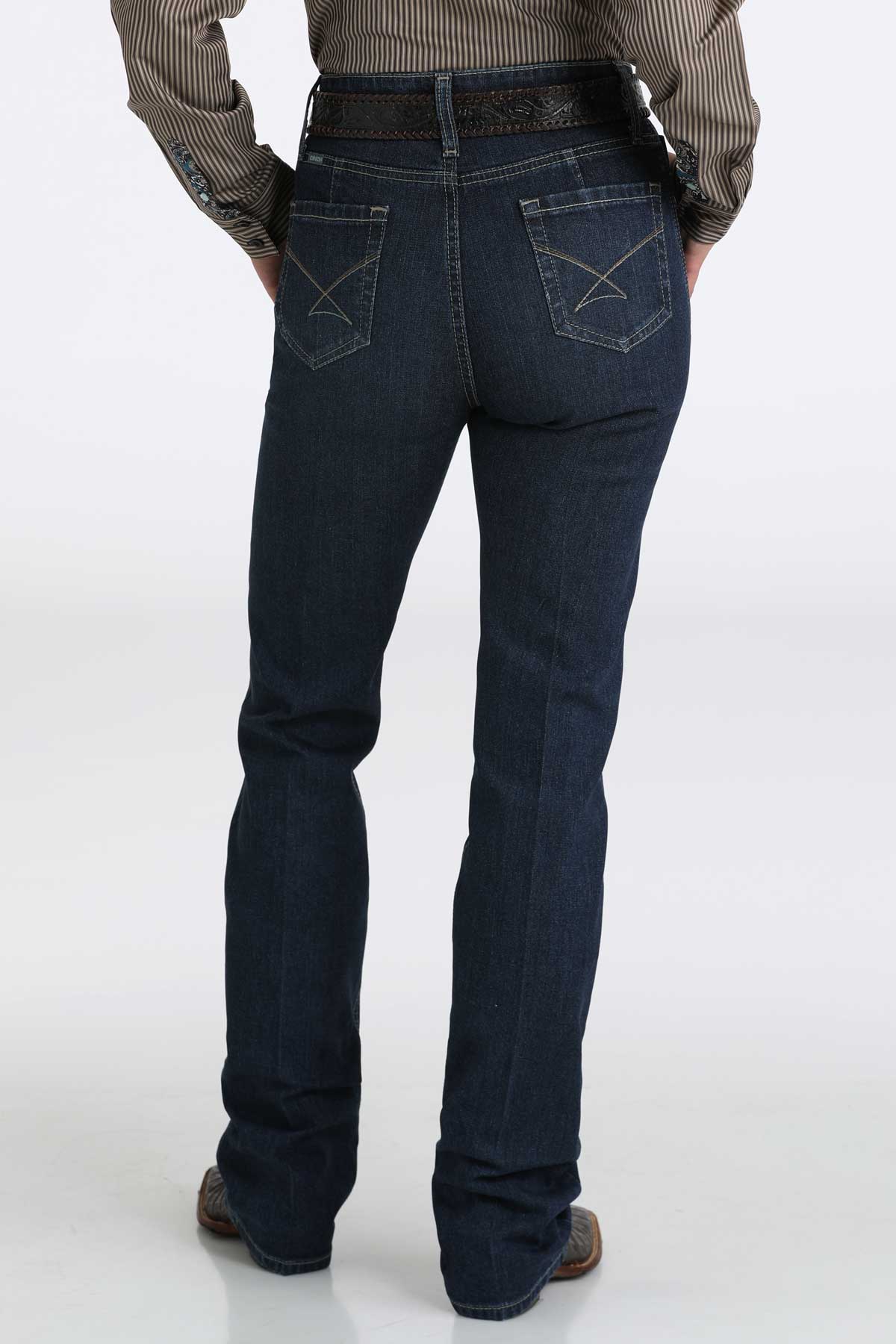 Back view of a woman wearing dark wash bootcut jeans with a belt and cowboy boots