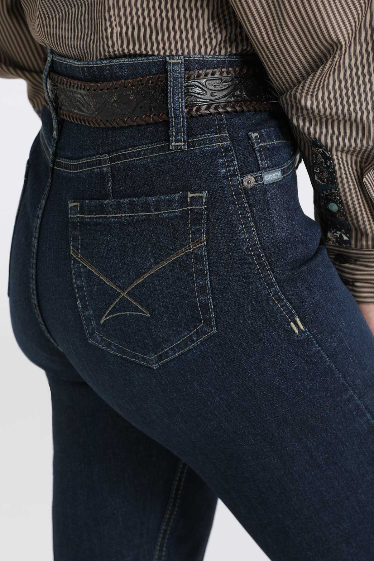 Close-up, back view of a woman wearing dark wash bootcut jeans with a belt and a shirt tucked in