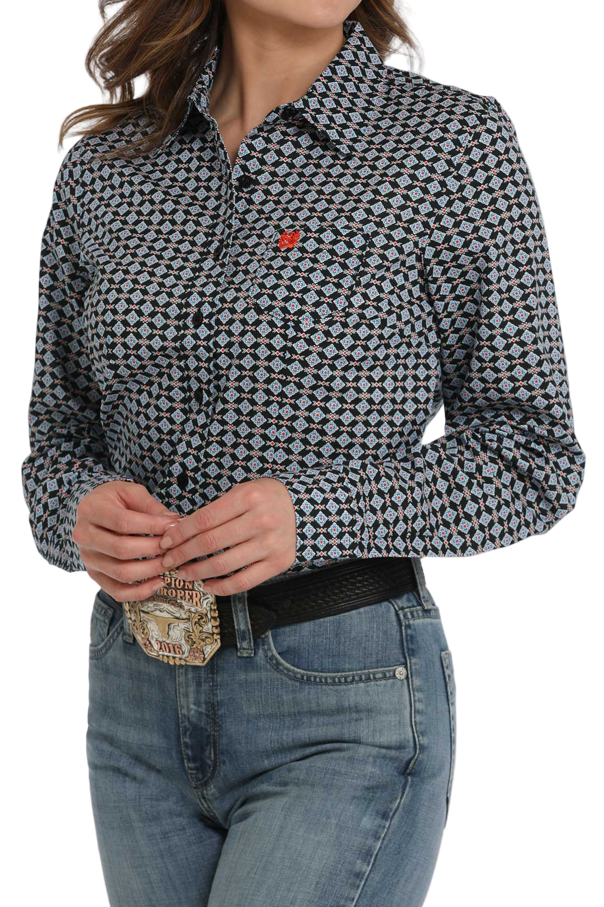 Woman wearing a patterned button-down shirt with a small red logo on the chest, paired with light-wash jeans and a western belt.