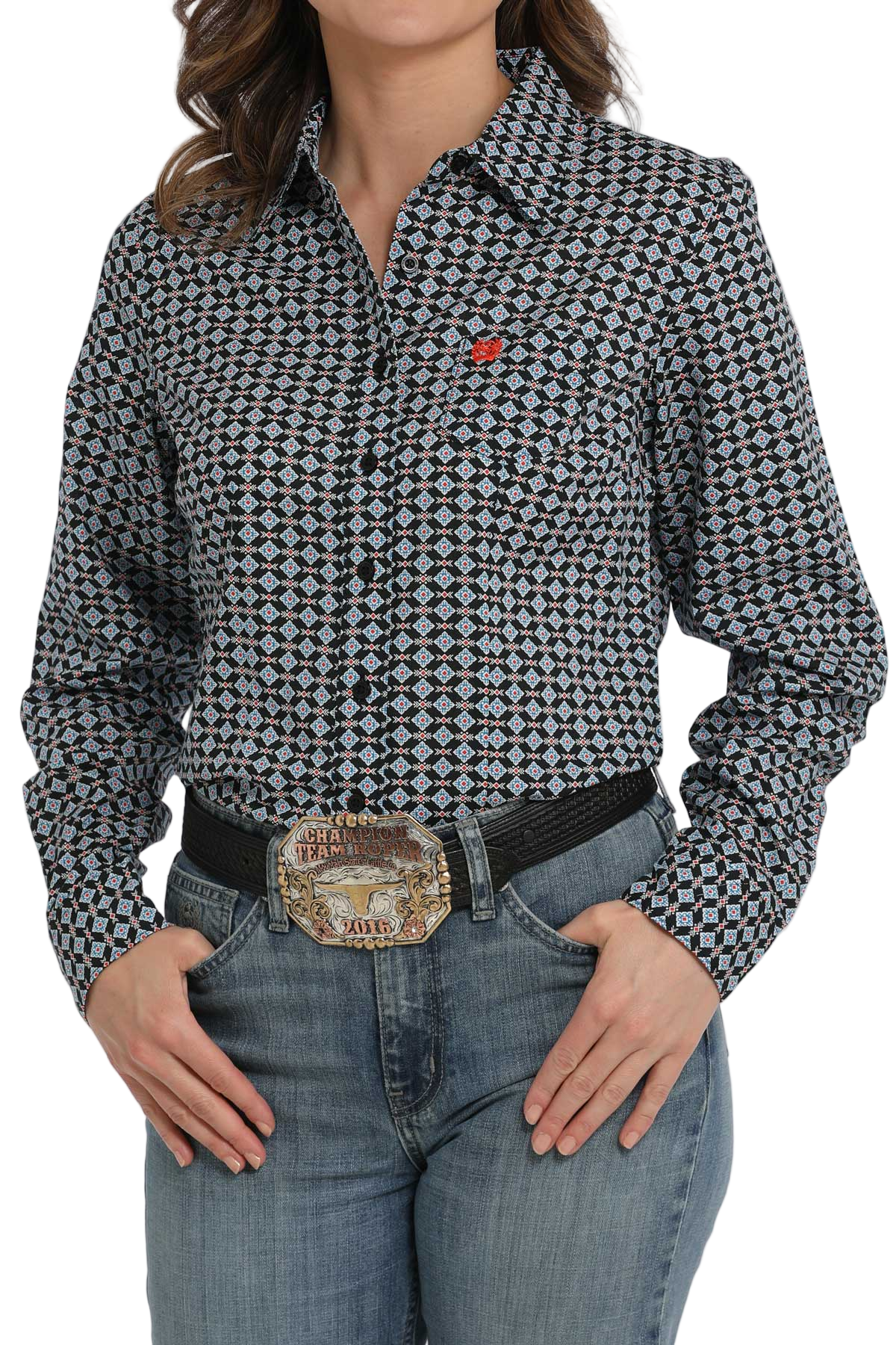 Woman wearing a patterned button-down shirt with a small red logo on the chest, paired with light-wash jeans and a western belt.