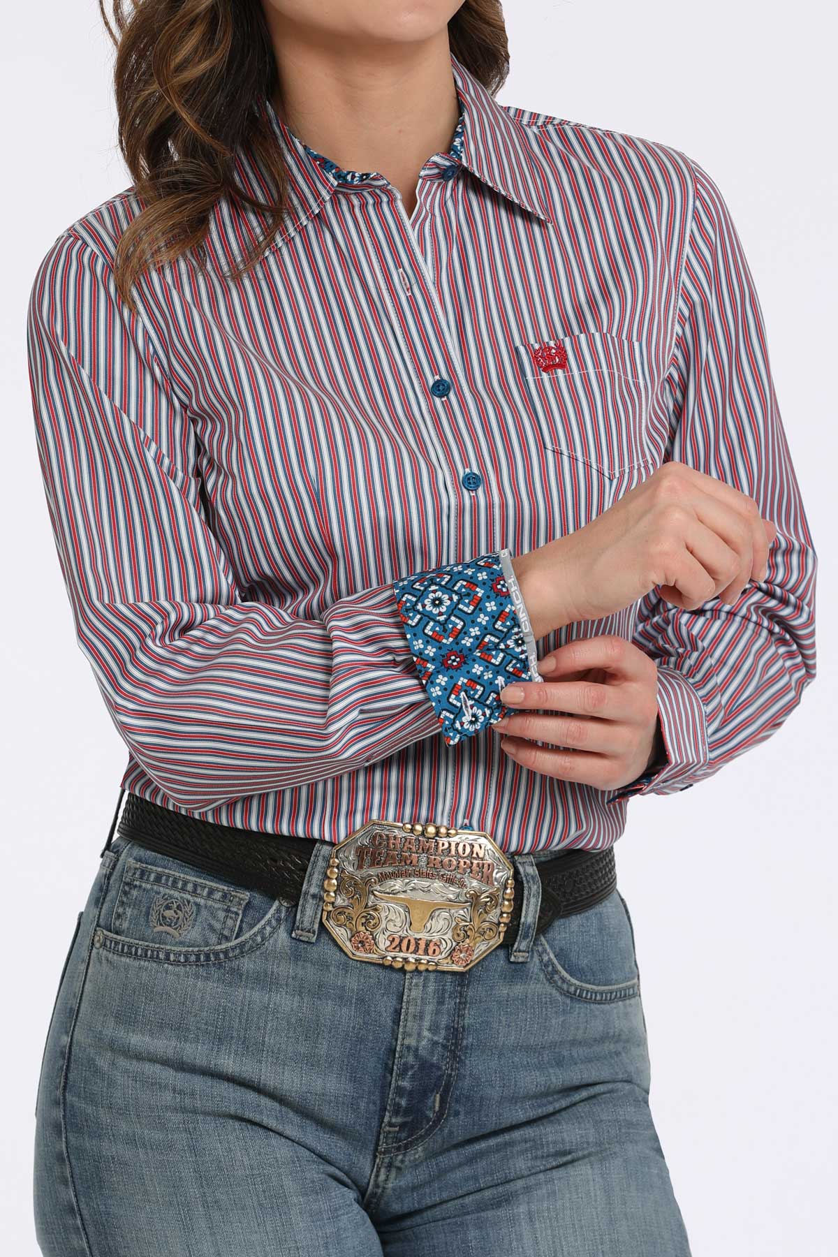 Person wearing a striped shirt with a colorful pattern on the cuffs, paired with jeans and a belt with a large buckle.