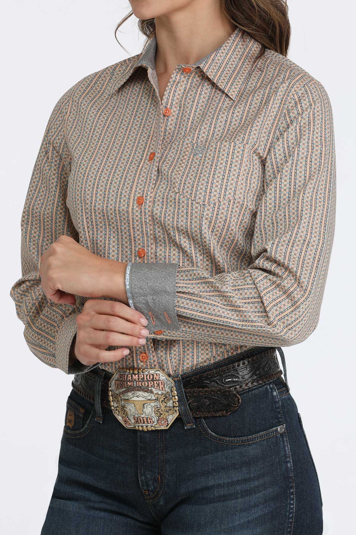 Woman wearing a brown long sleeve button-down with contrasting cuffs, paired with jeans and a belt
