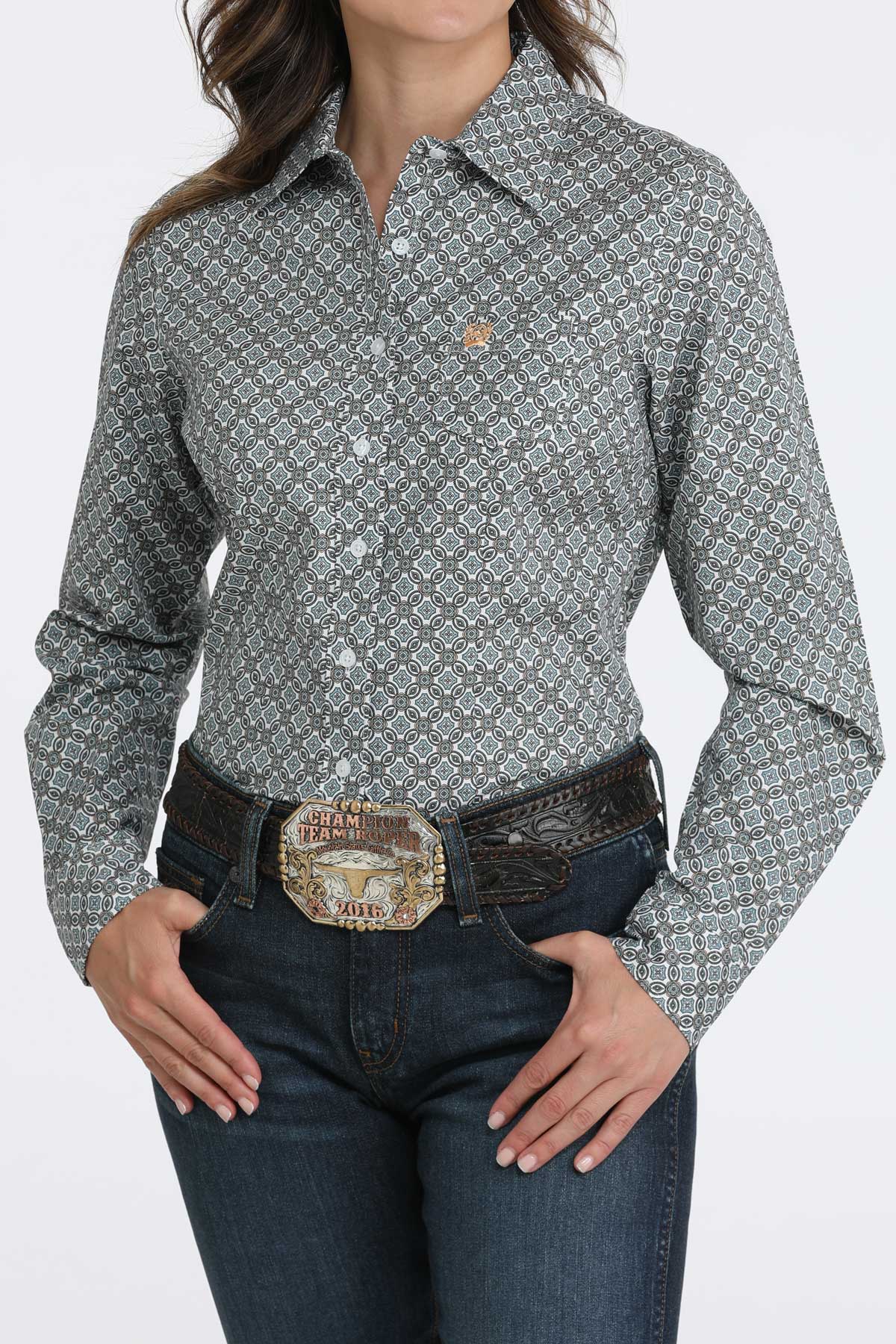 Woman wearing a Cinch ladies’ long sleeve white print shirt tucked into jeans with a large western belt buckle on a white background