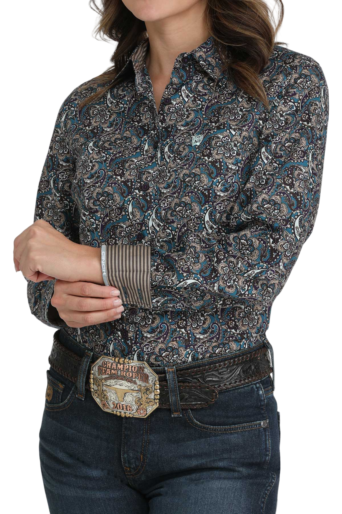 Woman wearing a patterned button-down shirt with striped contrast cuffs, paired with jeans and a western-style belt buckle
