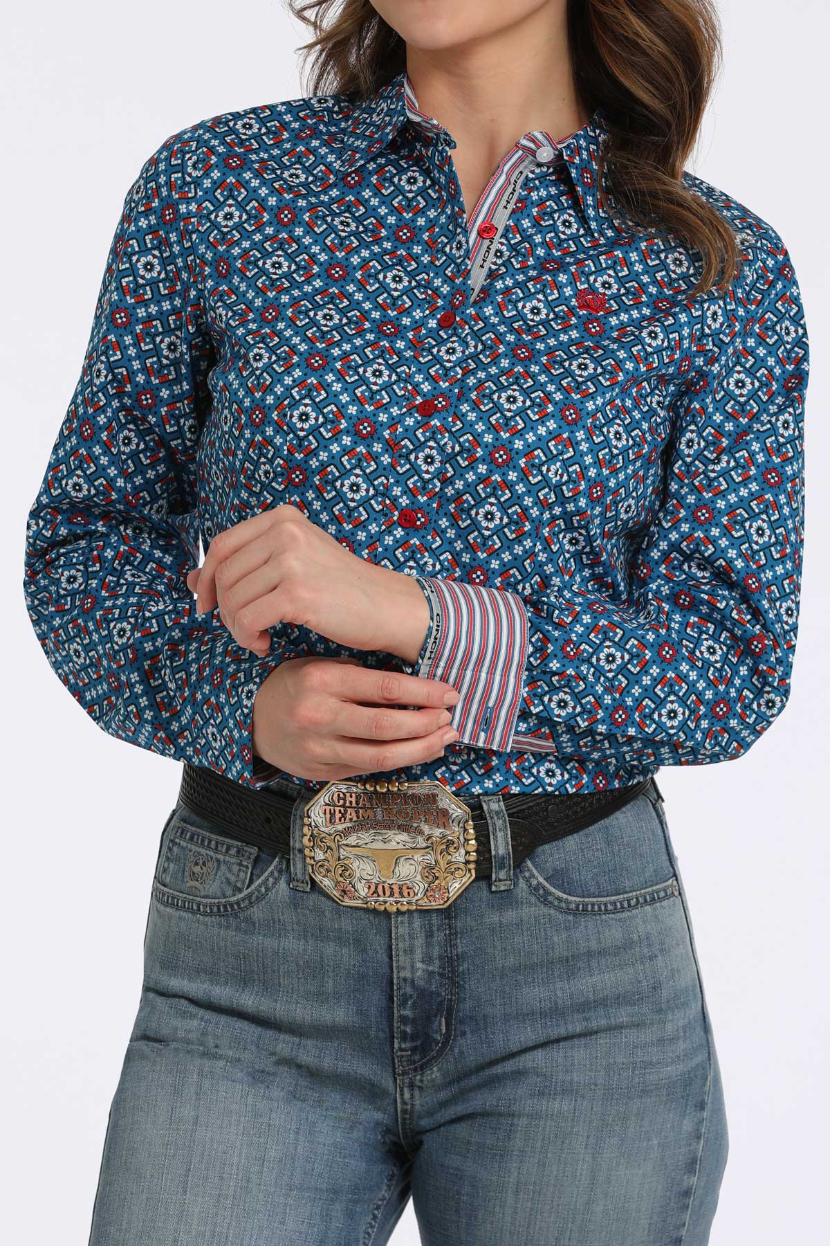 Woman wearing a blue long sleeve button-down with a geometric pattern, with contrasting red cuffs, paired with jeans and a belt