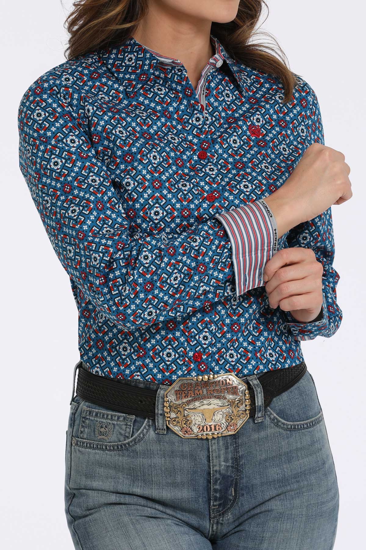 Woman wearing a blue long sleeve button-down with a geometric pattern, with contrasting red cuffs, paired with jeans and a belt