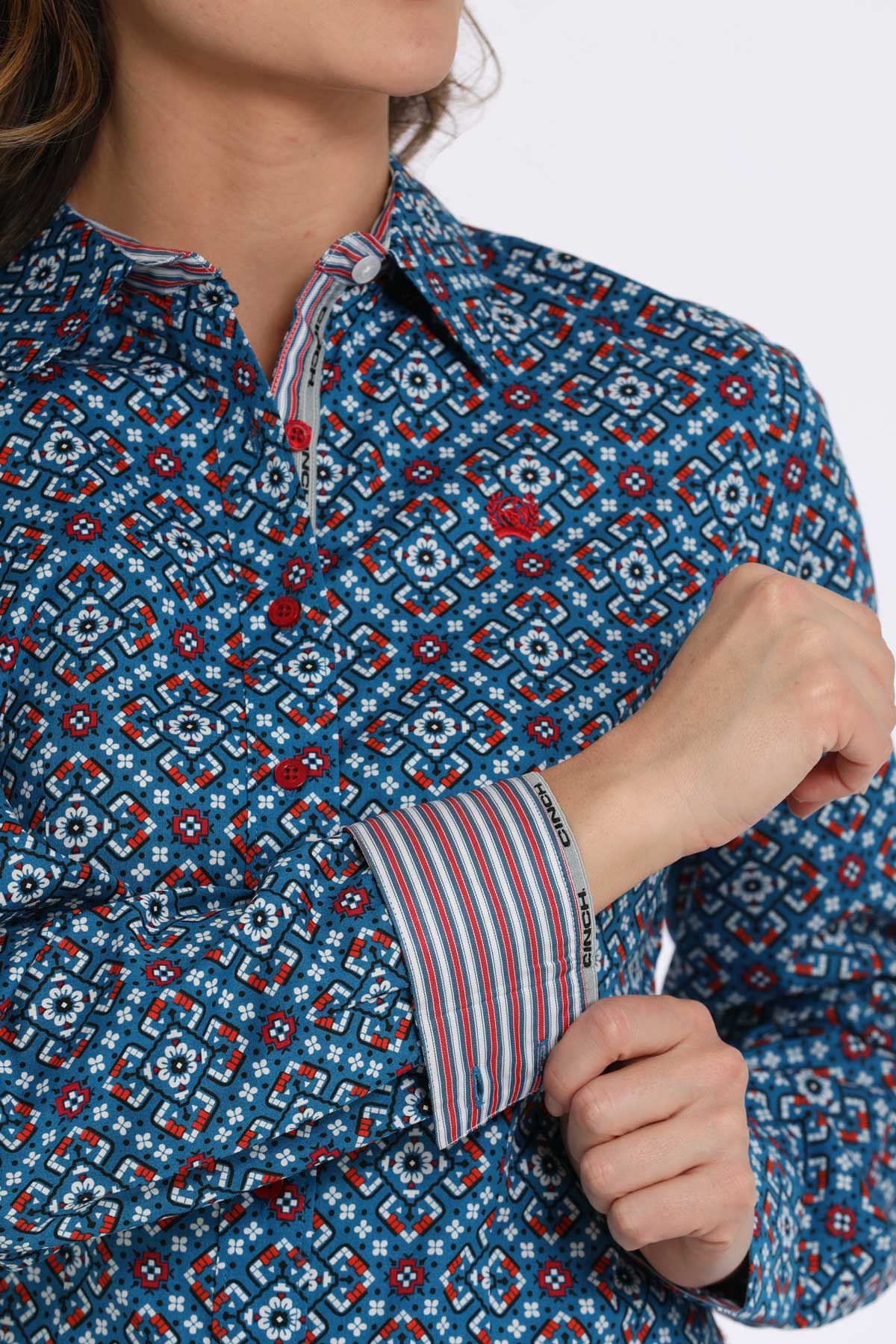 Woman wearing a blue long sleeve button-down with a geometric pattern, with contrasting red cuffs