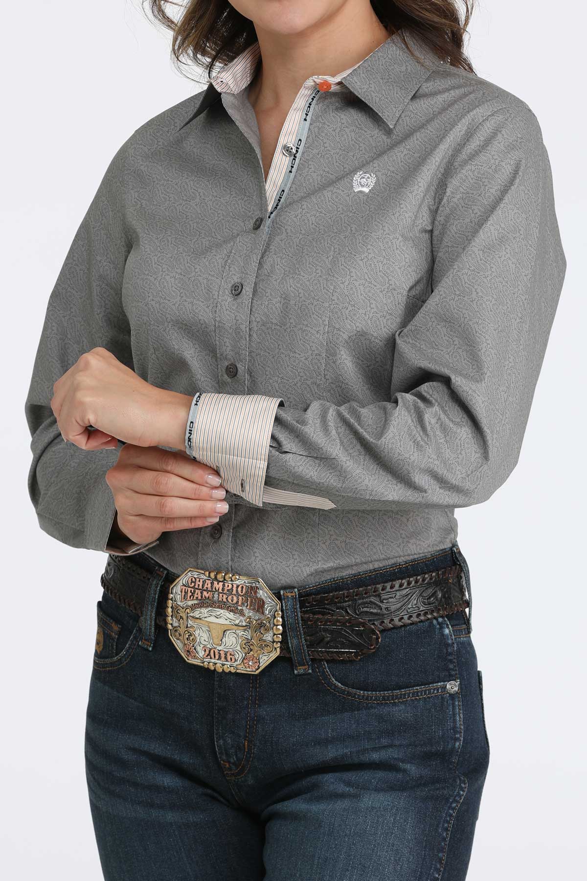 Person wearing a gray button-up shirt, jeans, and a belt with a large buckle on a white background
