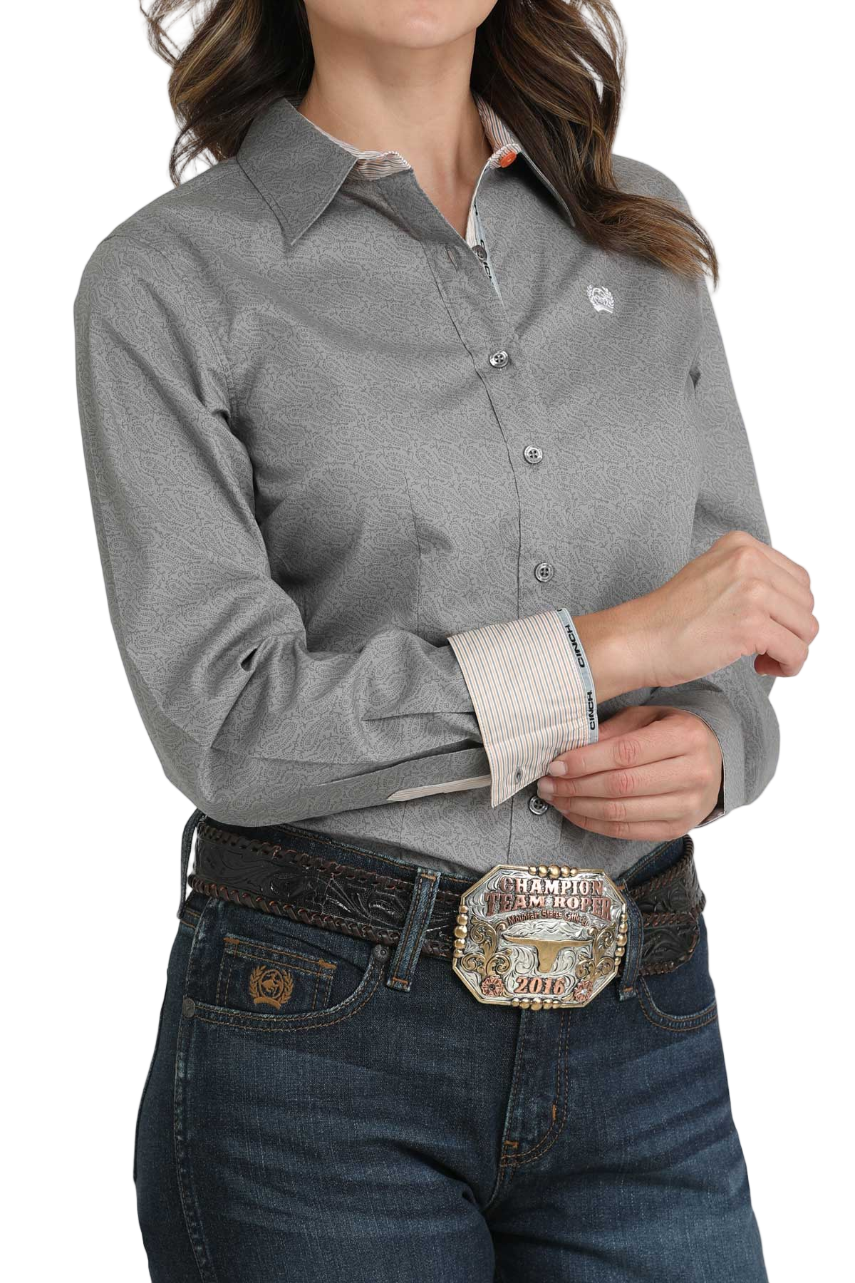 Woman wearing a gray long-sleeve button-down shirt with contrasting cuffs, paired with jeans and a large western belt buckle