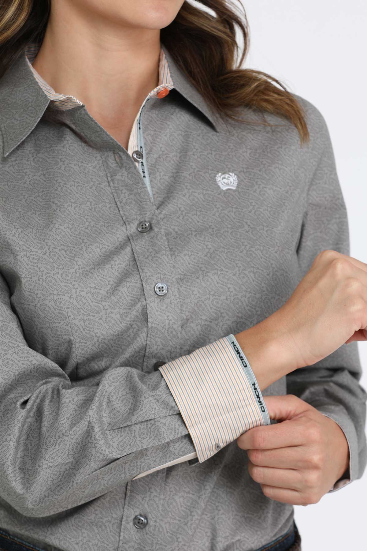 Person wearing a gray button-up shirt with a brand logo on a white background