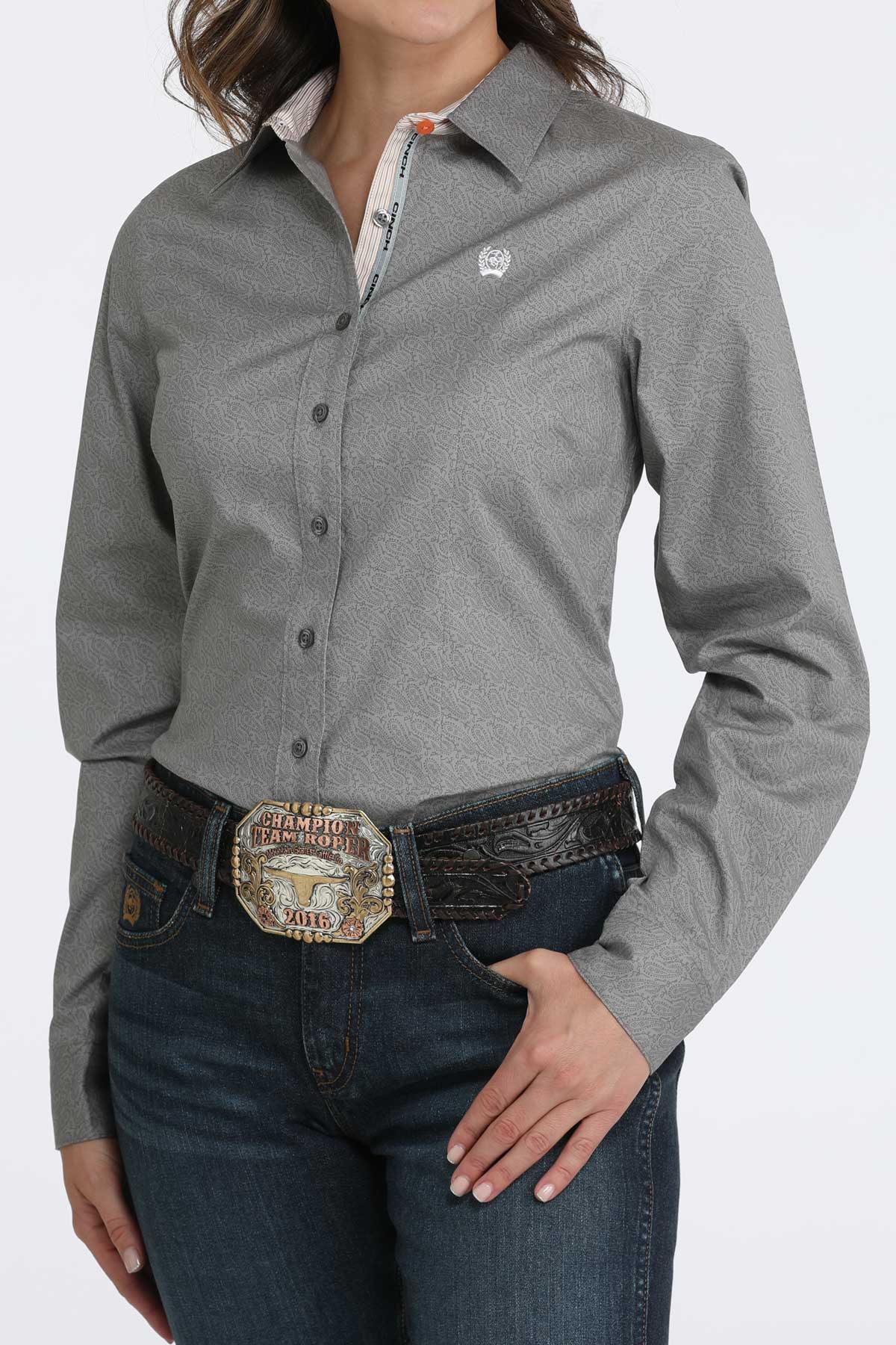 Person wearing a gray button-up shirt with a belt and jeans on a white background
