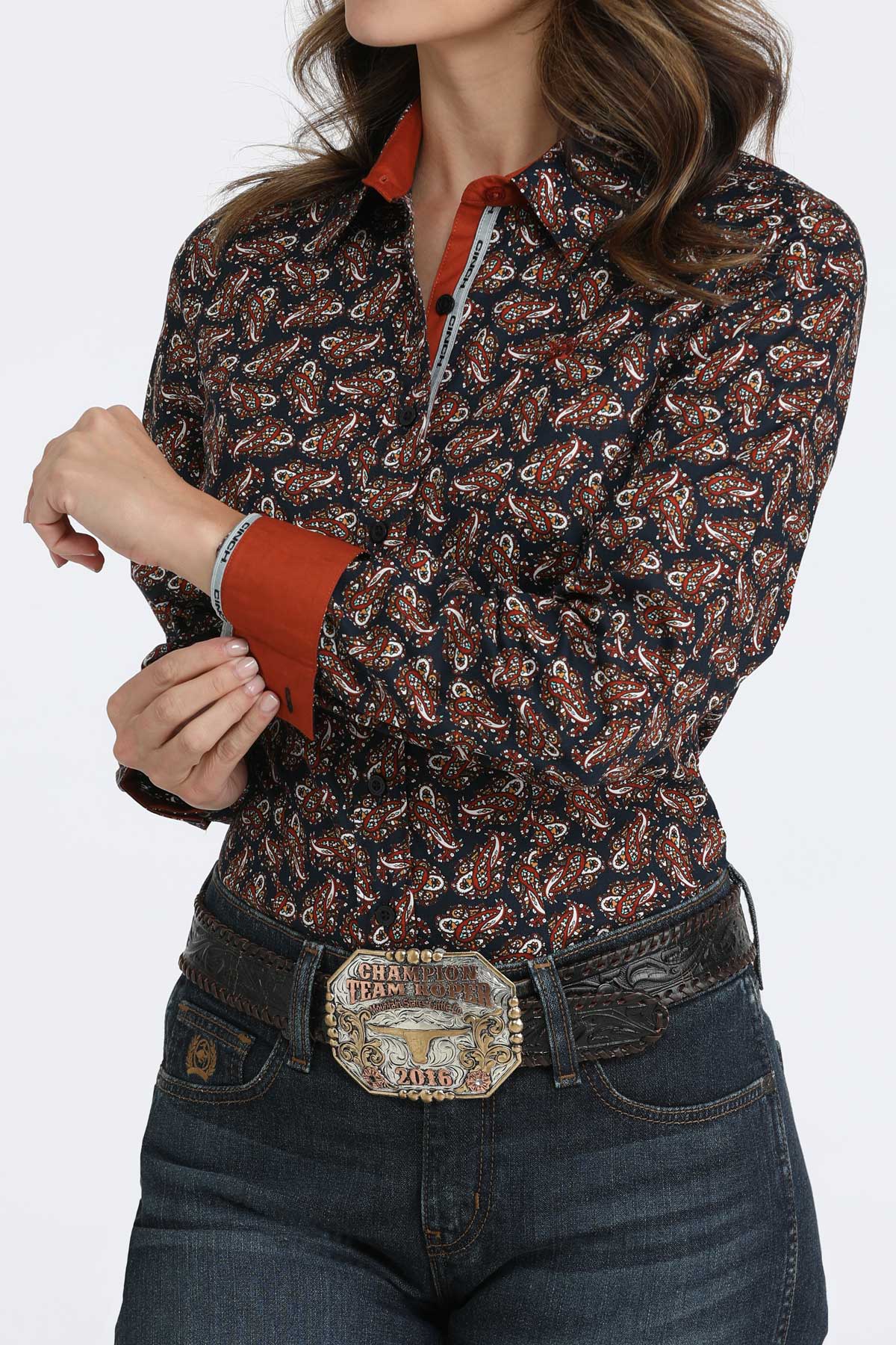 Woman wearing a long sleeve button-down that features contrasting cuffs, paired with a belt and jeans