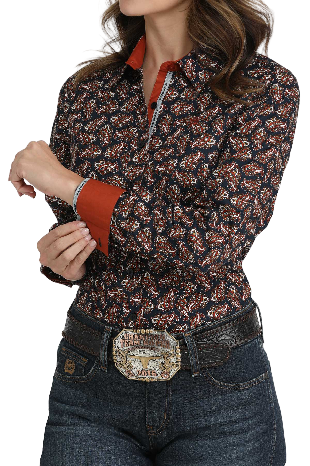 Woman wearing a dark patterned button-down shirt with solid red contrast cuffs and collar, paired with a tooled belt and dark denim jeans