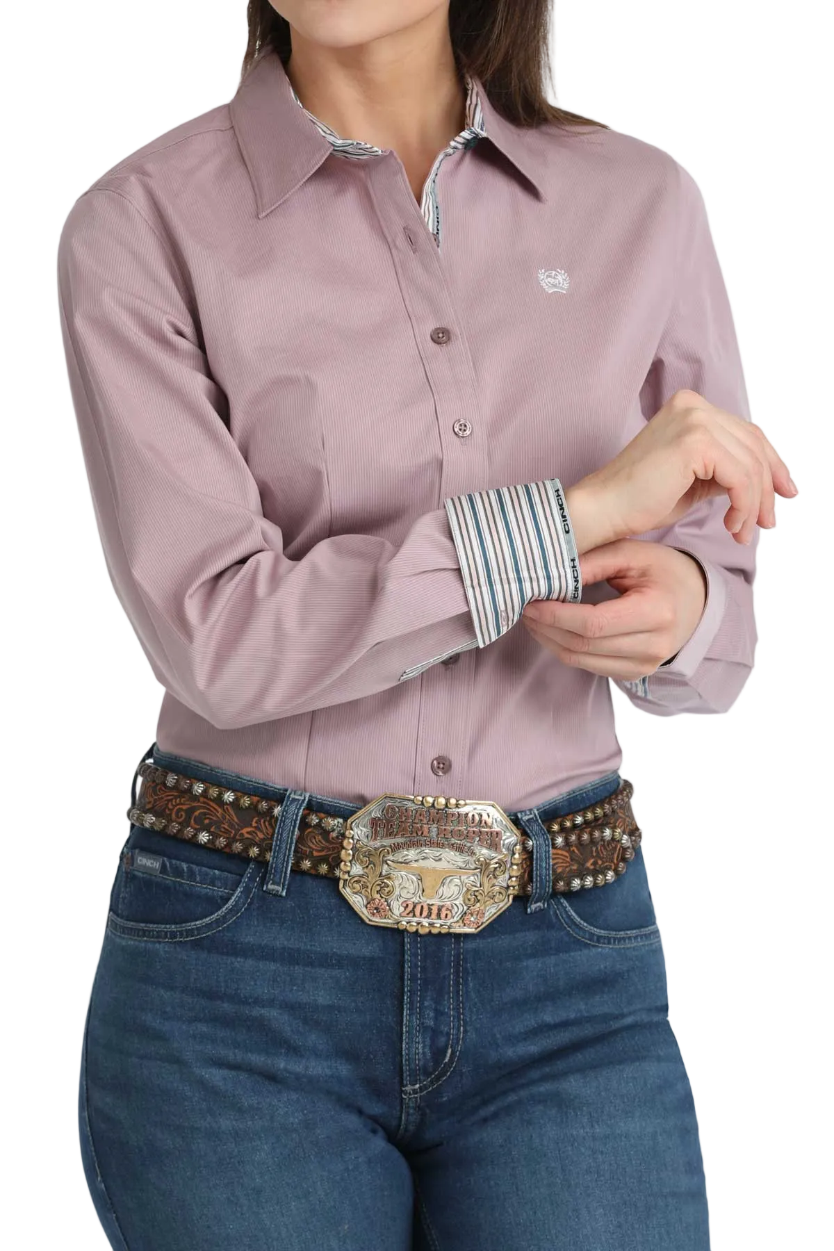 Woman wearing a mauve button-up shirt and blue jeans with a large belt buckle.