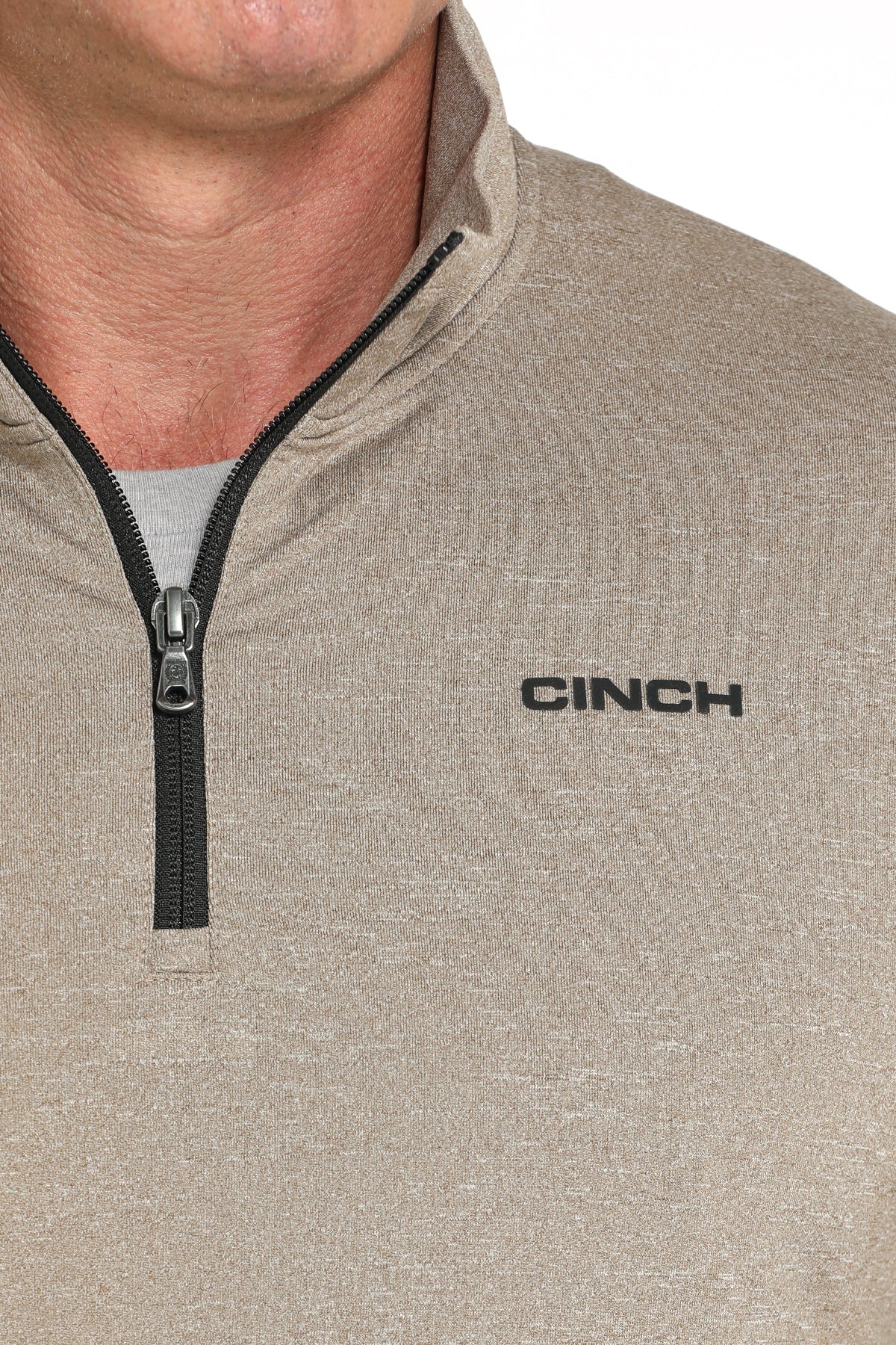 Close-up view of a beige CINCH quarter-zip pullover with a black zipper and logo displayed on a white background.