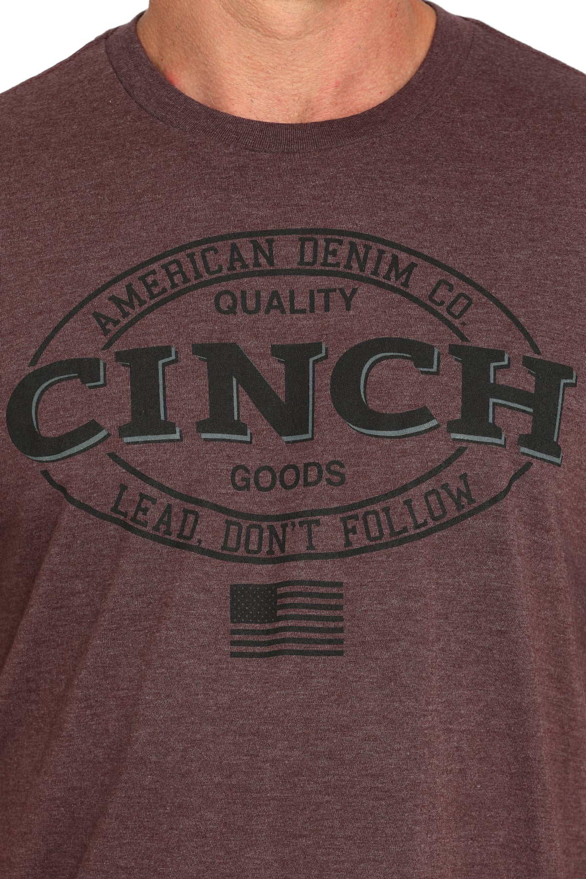Close-up of a man wearing a brown t-shirt with a large 'Cinch' graphic on the front on a white background