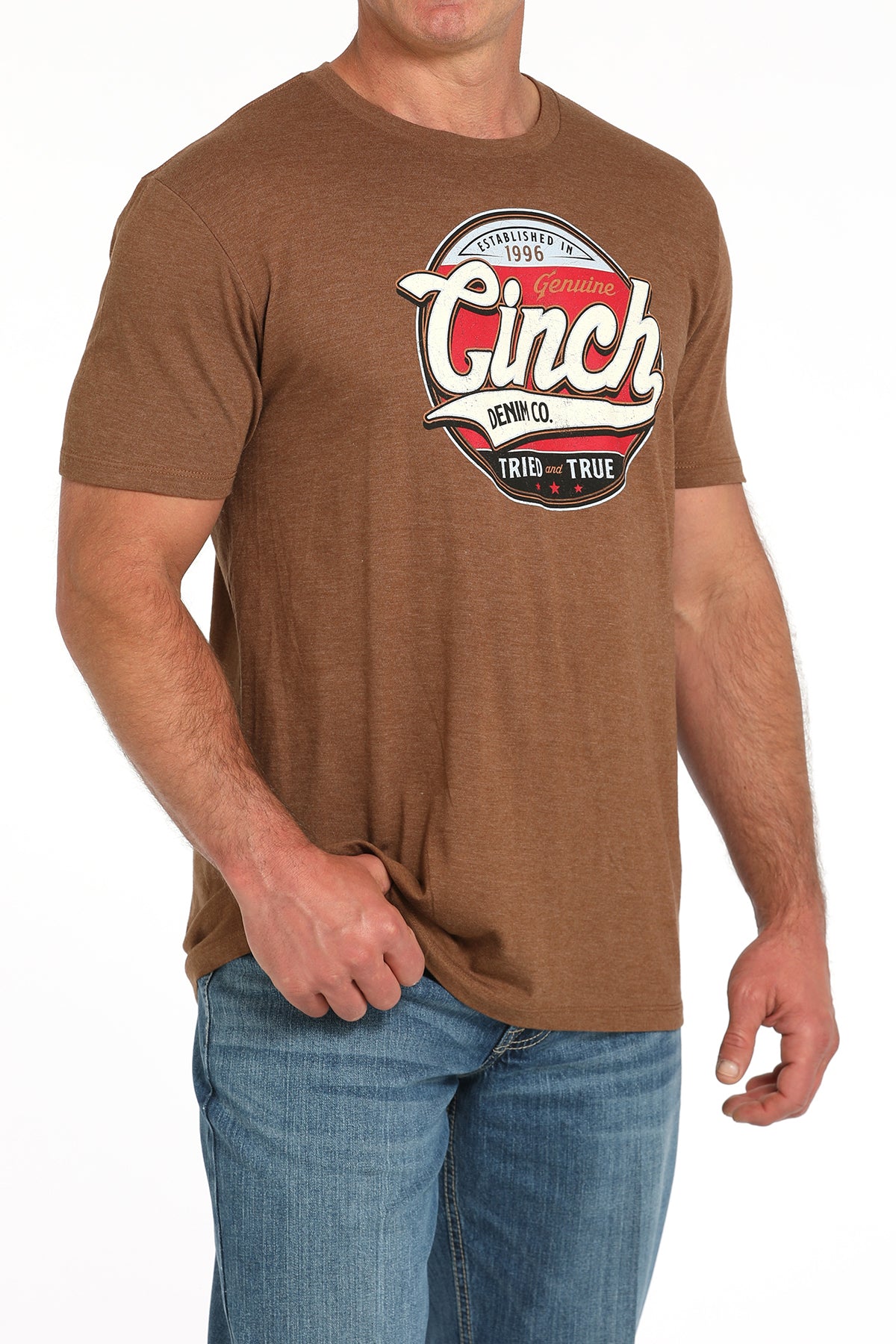 Man wearing a brown t-shirt with a large 'Cinch' graphic on the front and blue jeans on a white background