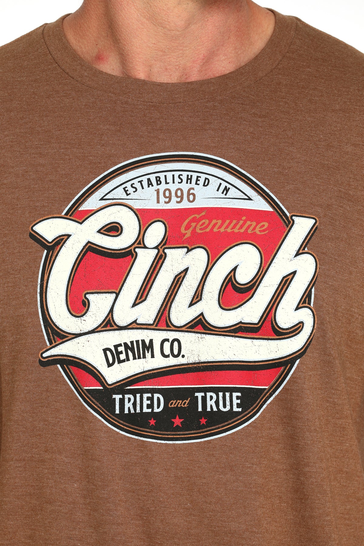 Close-up of a man wearing a brown t-shirt with a large 'Cinch' graphic on the front on a white background