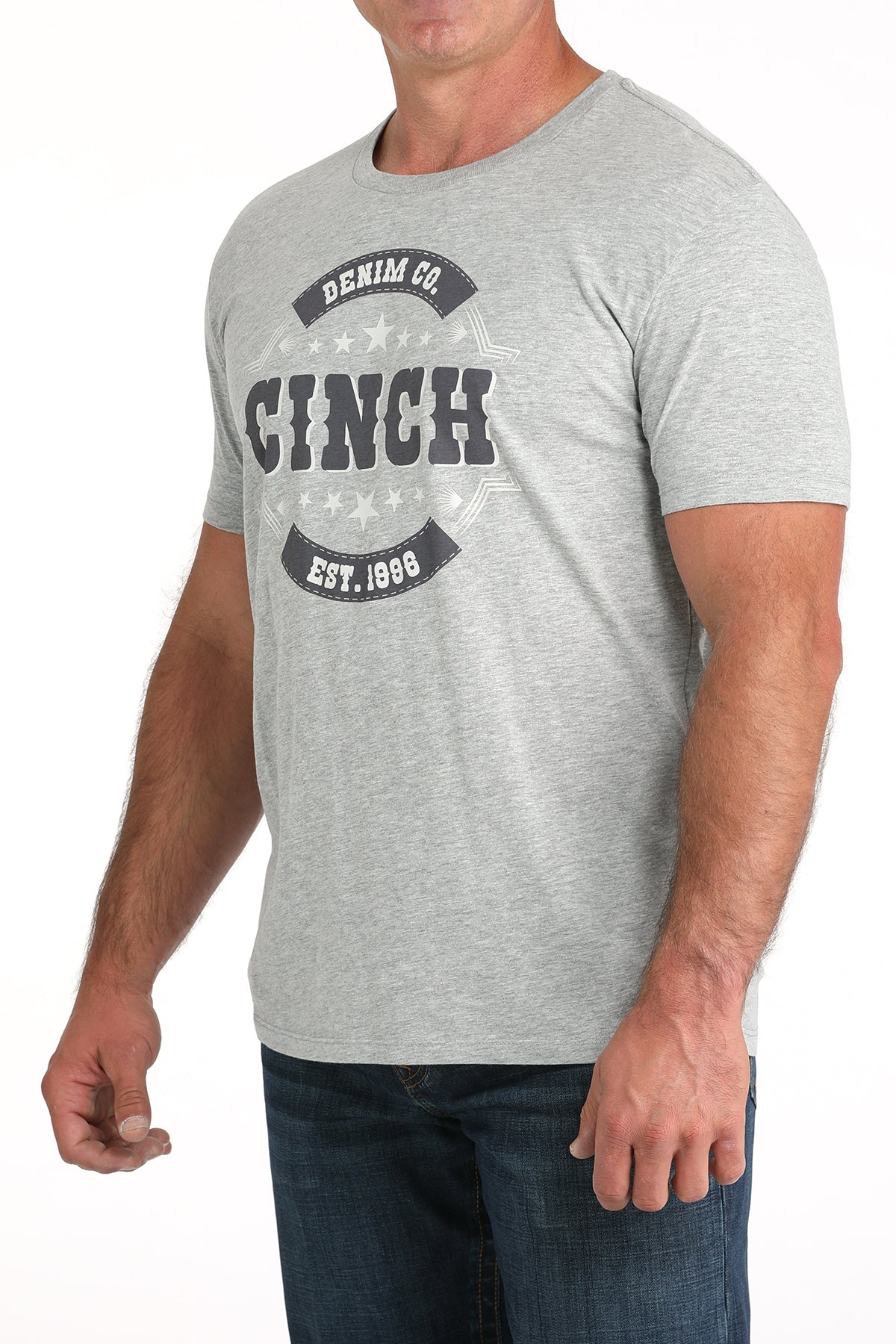 Man wearing a light gray t-shirt with a large 'Cinch' graphic on the front and blue jeans on a white background