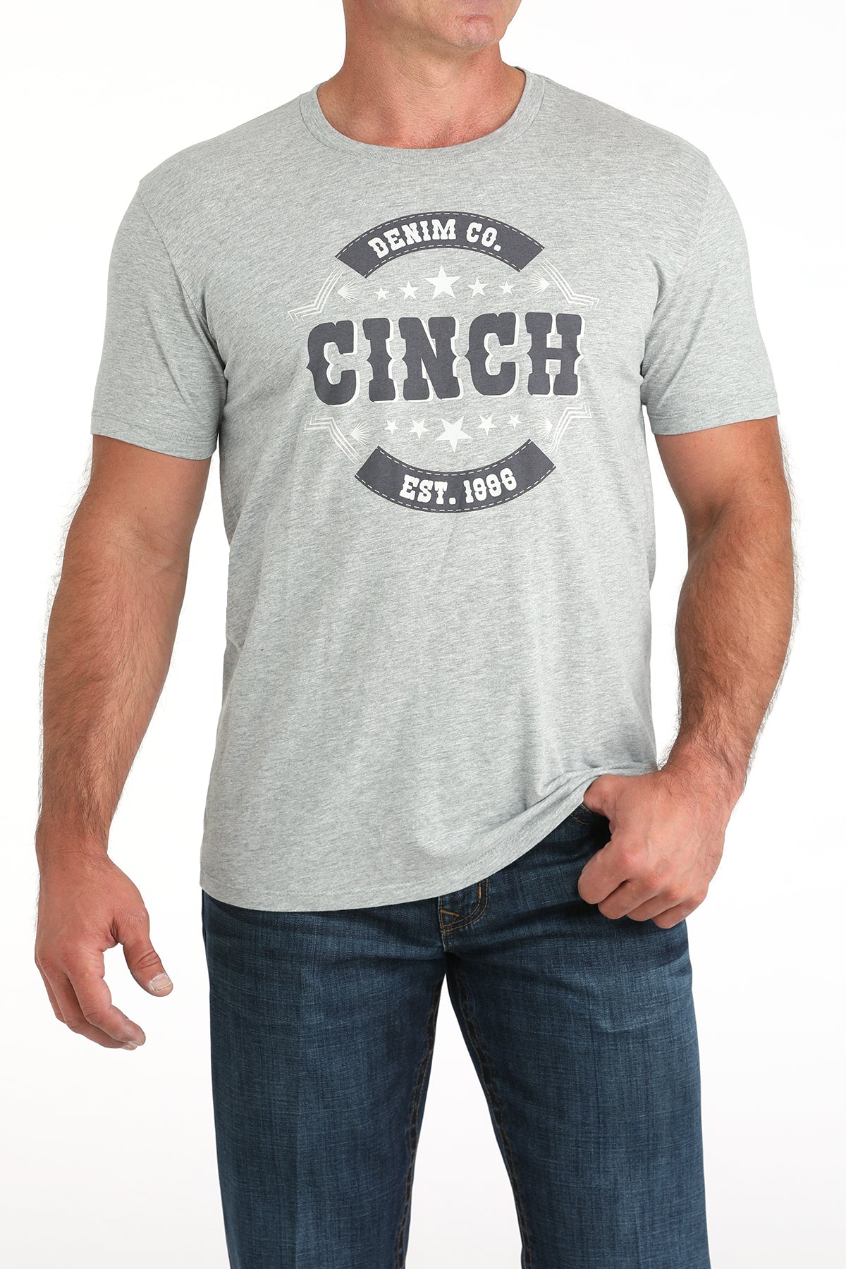 Man wearing a light gray t-shirt with a large 'Cinch' graphic on the front and blue jeans on a white background