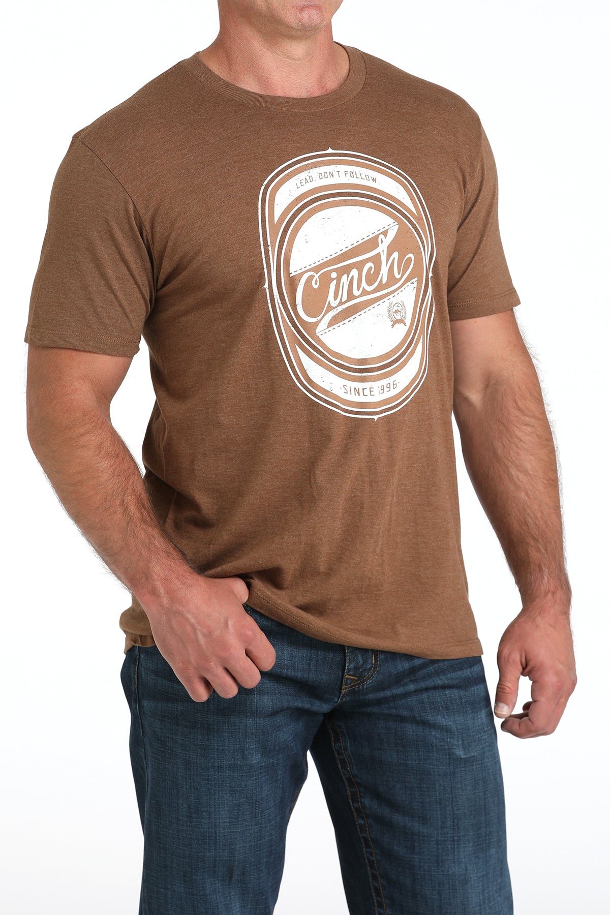 Man wearing a brown t-shirt with a logo and text, standing against a white background