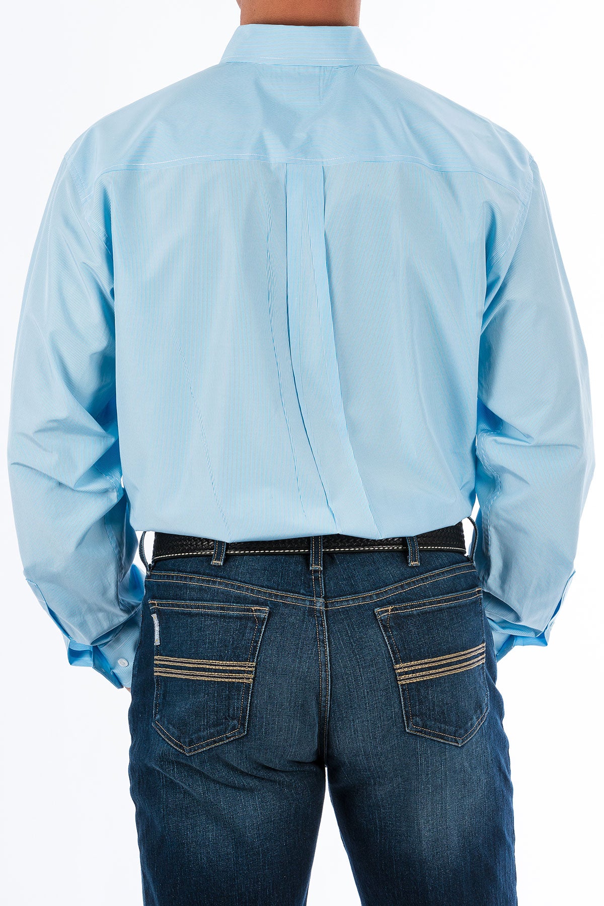 Back view of a man wearing a light blue, long sleeve, button-down shirt, with jeans and a western belt