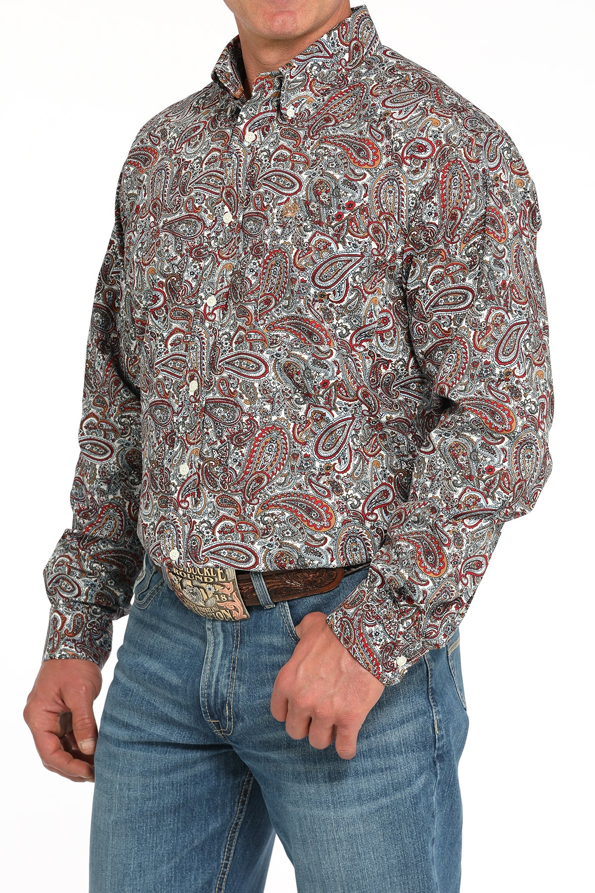 Man wearing a long sleeve button-down shirt with an all-over paisley pattern, paired with jeans and a belt
