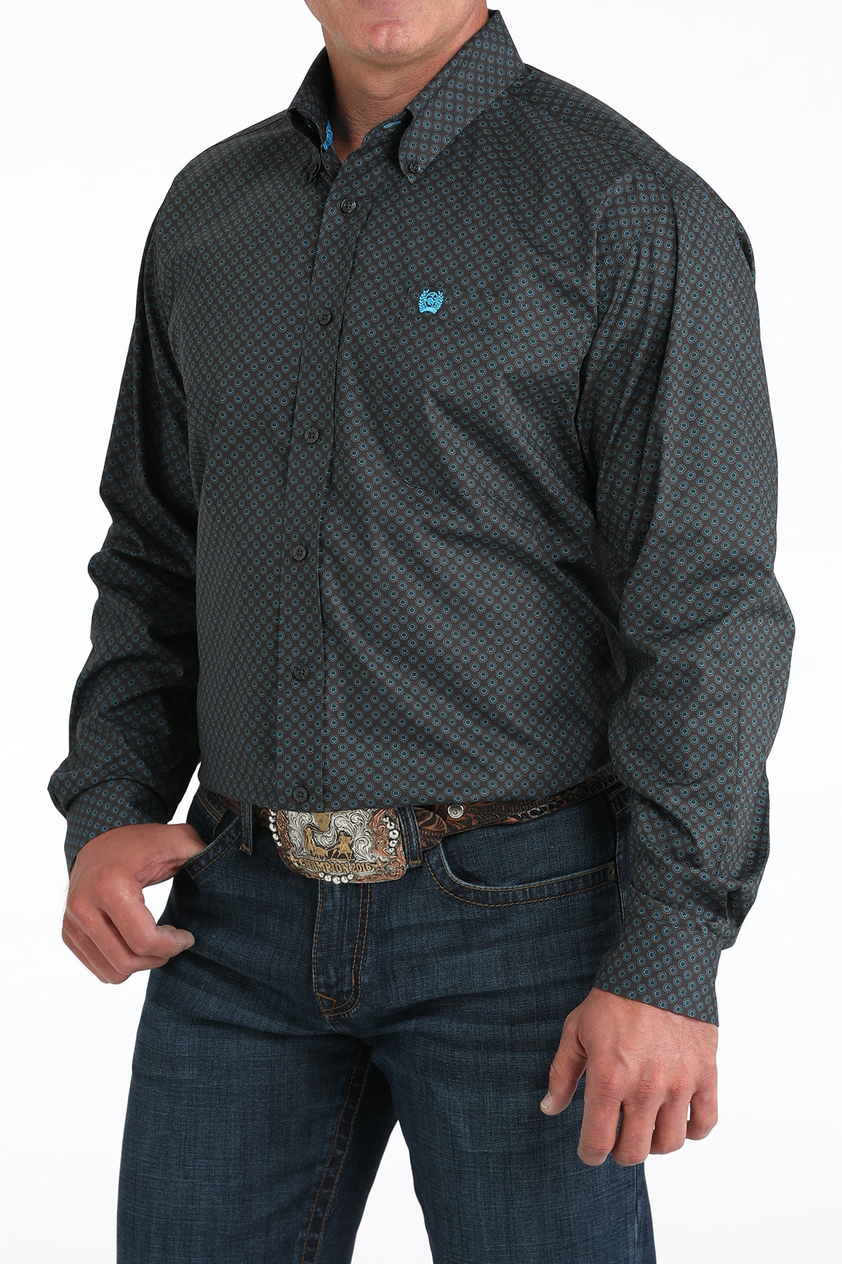 Man wearing a patterned gray shirt and jeans with a belt buckle.