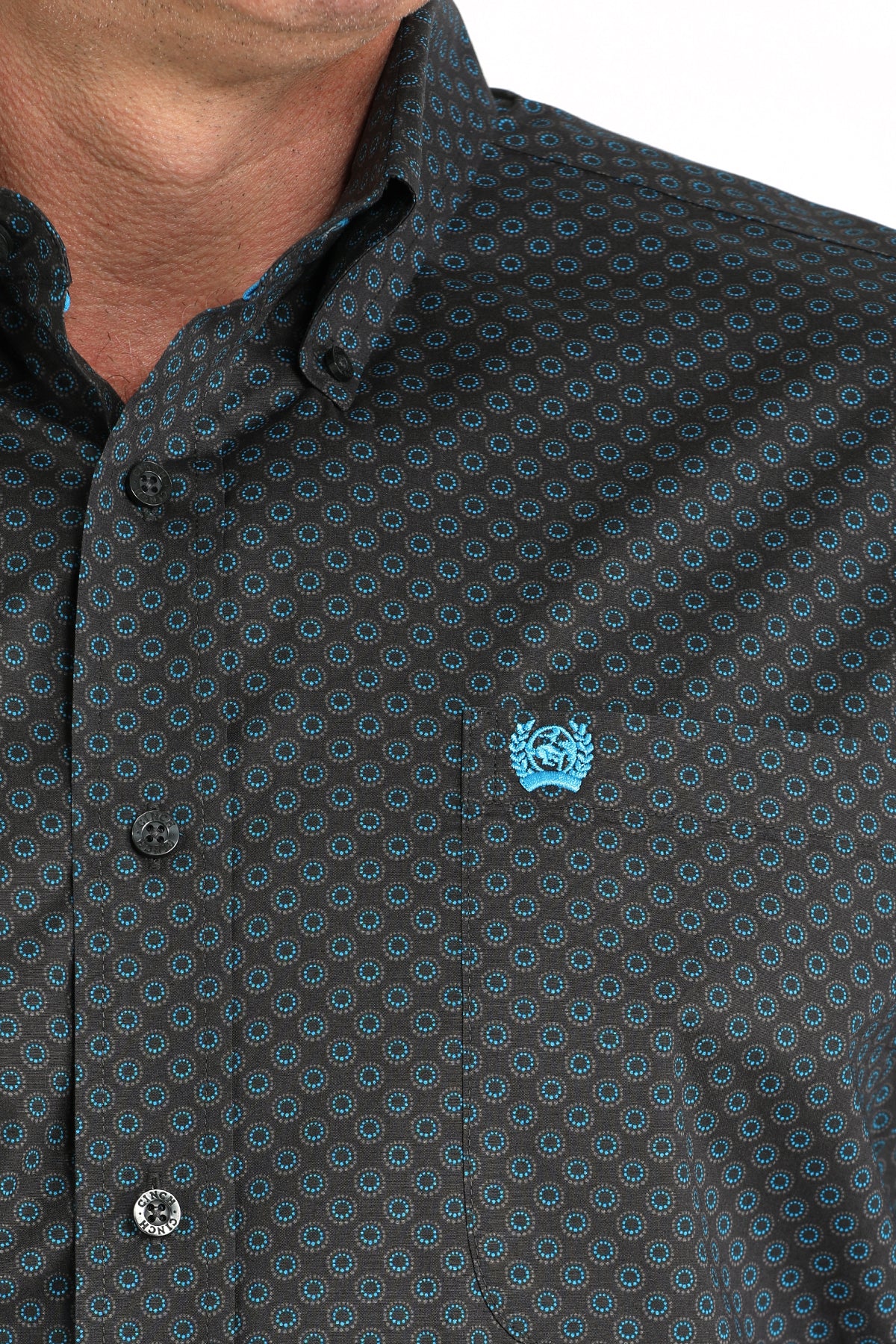 Close-up of a dark patterned shirt with a blue logo on a white background