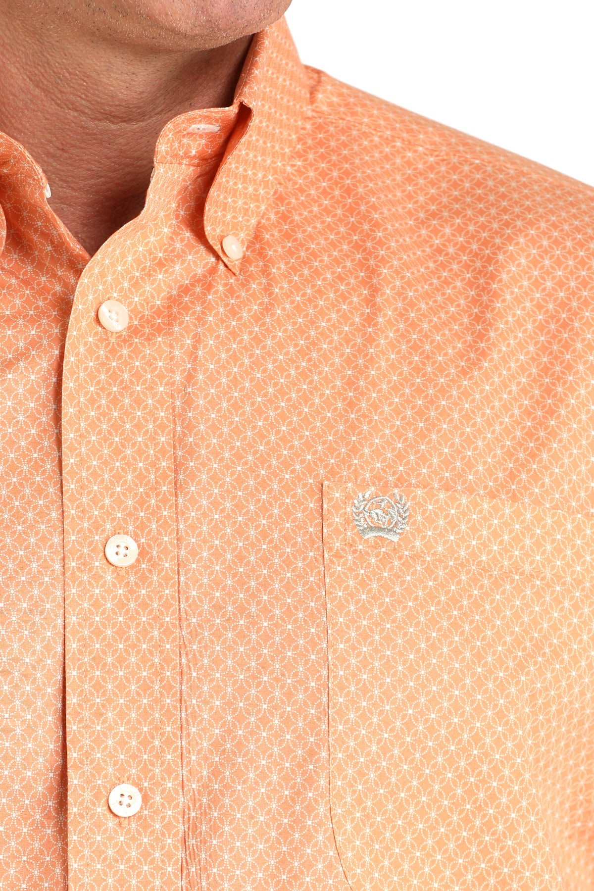 Close-up of an orange patterned shirt with a brand logo on a white background
