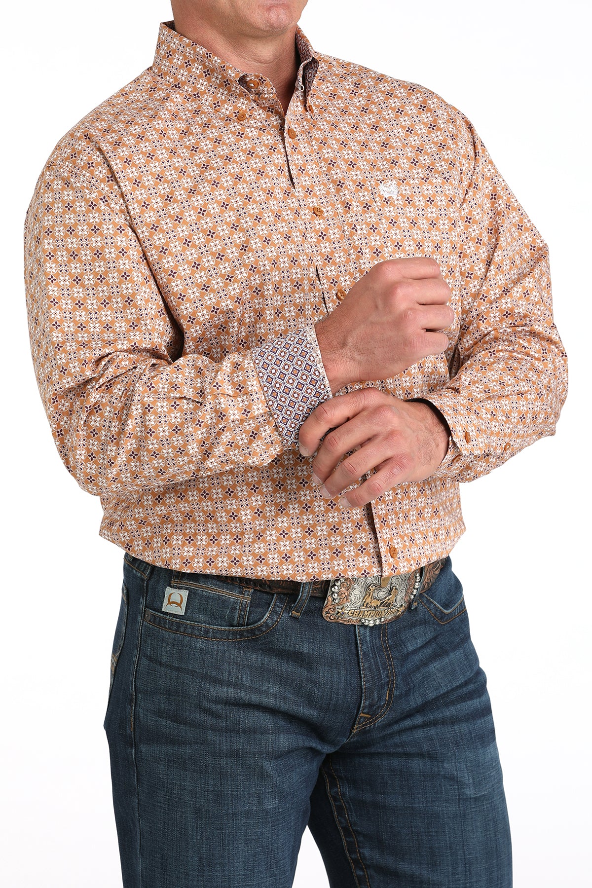 Man wearing a long sleeve button-down shirt that is brown and has a pattern, as well as contrasting cuffs, paired with jeans and a belt