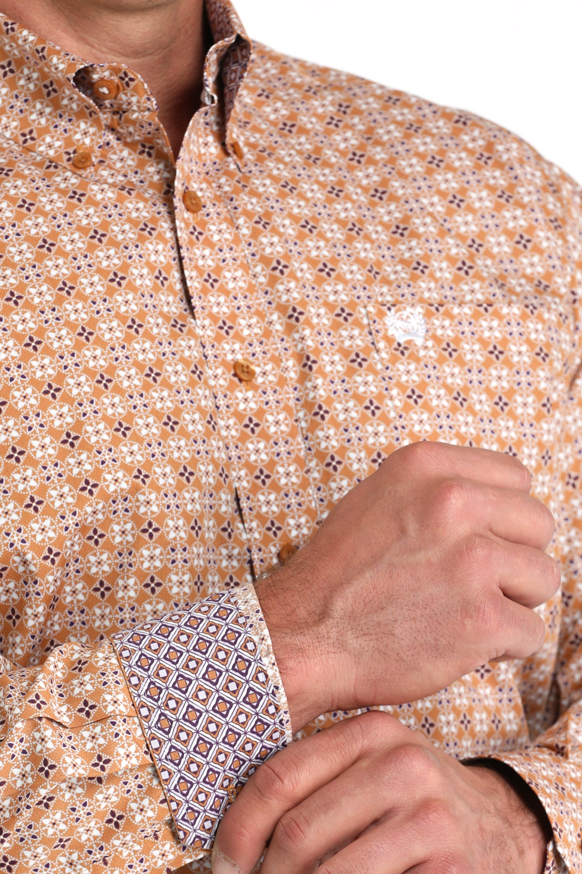 Close-up of a man wearing a long sleeve button-down shirt that is brown and has a pattern, that also as contrasting cuffs