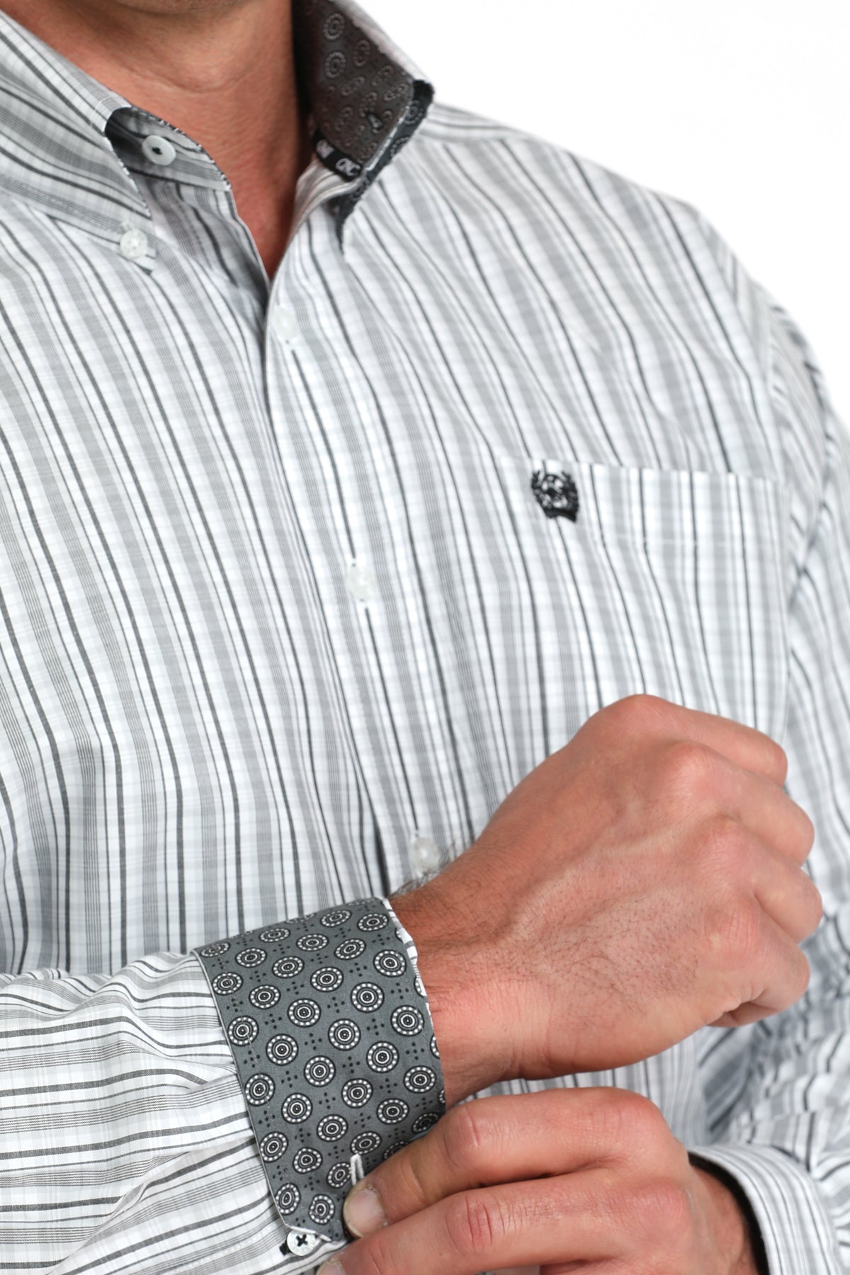 Close-up of a man wearing a light, striped, long sleeve, button-down shirt with contrasting cuffs and a chest pocket