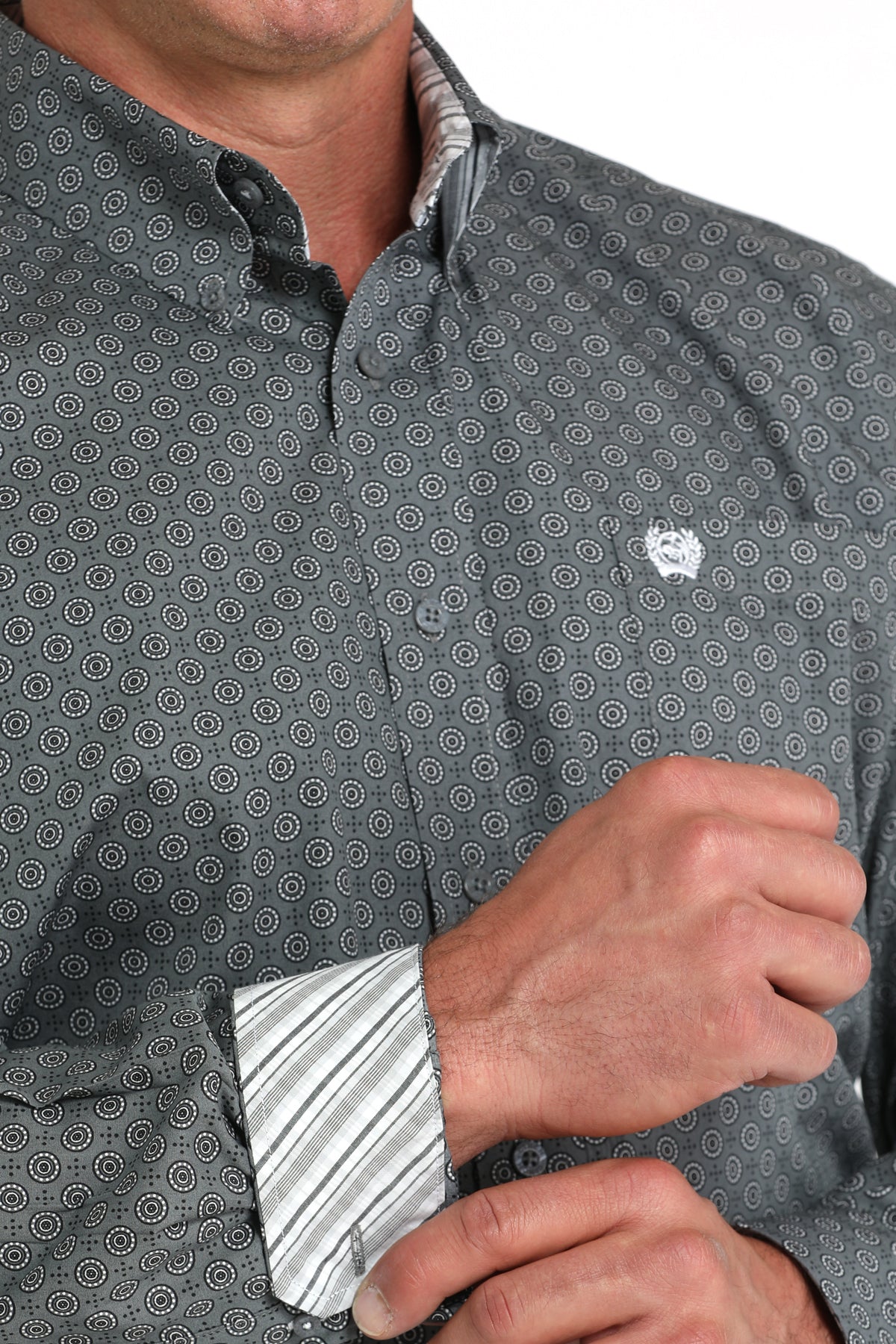 Close-up of a man wearing a gray, patterned, long sleeve, button-down shirt with contrasting cuffs and a chest pocket