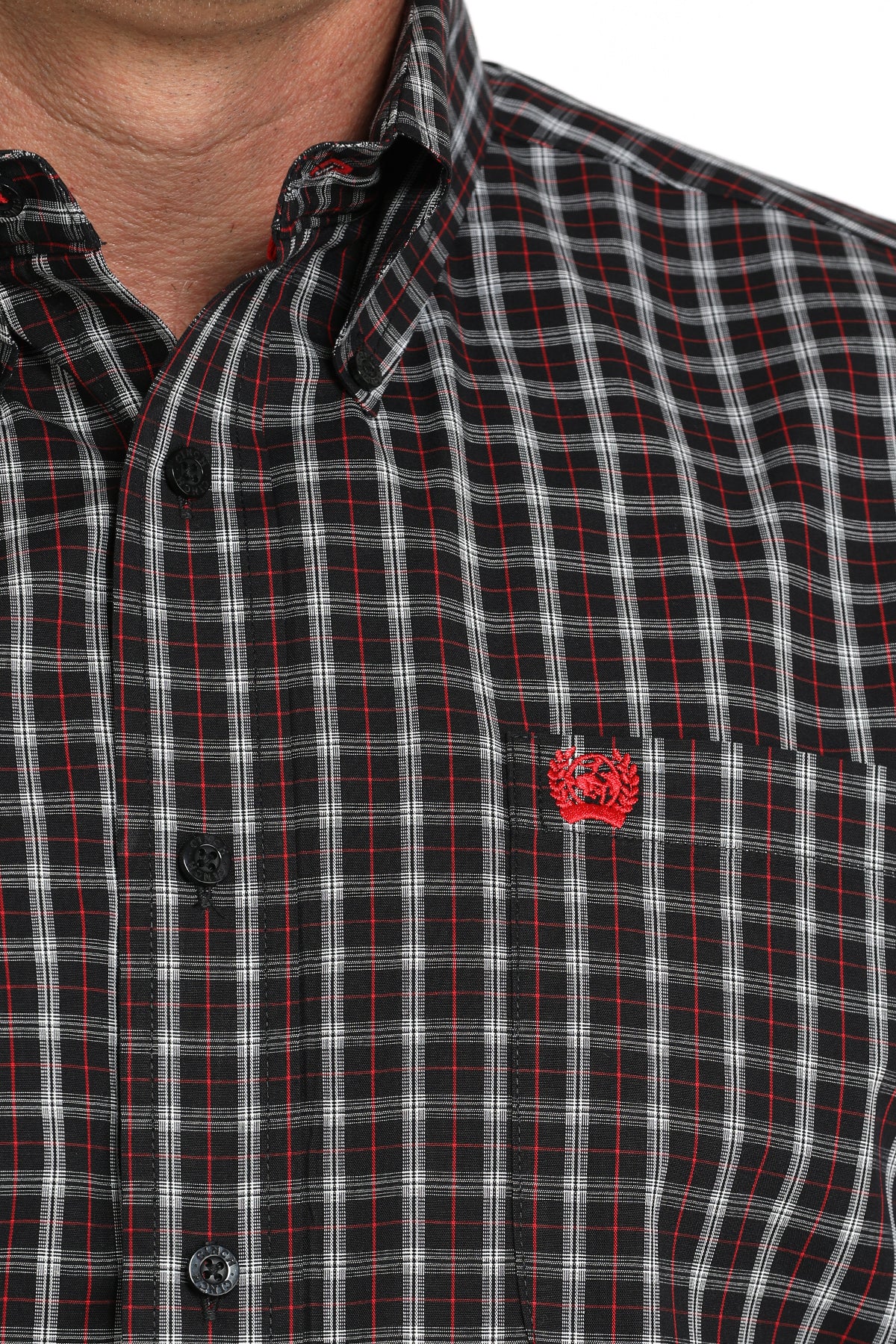 Close-up of a man wearing a brown patterned button-up shirt with a small red emblem on the chest, displayed against a white background
