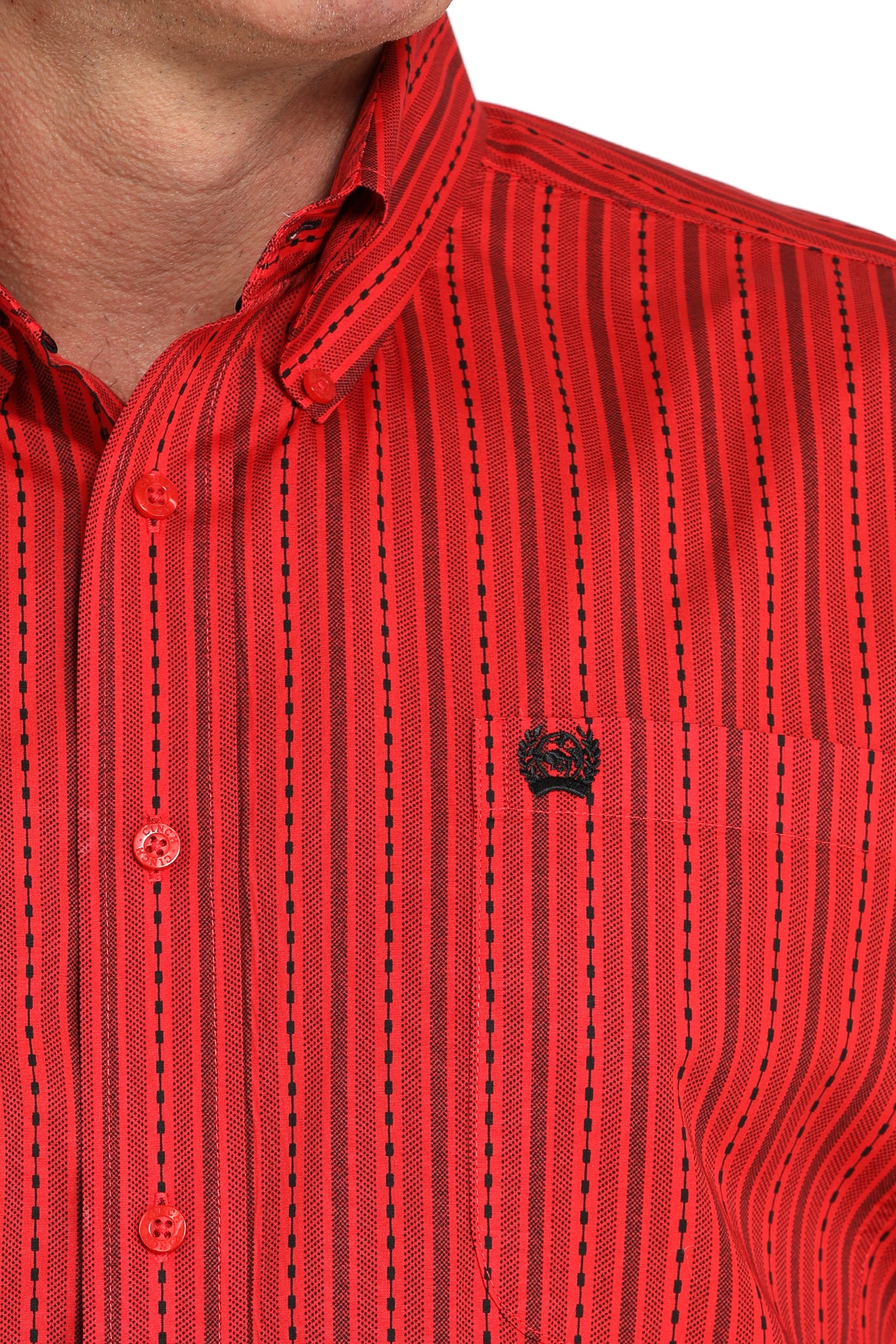 Close-up of a man wearing a red striped button-up shirt with a small black emblem on the chest, displayed against a white background