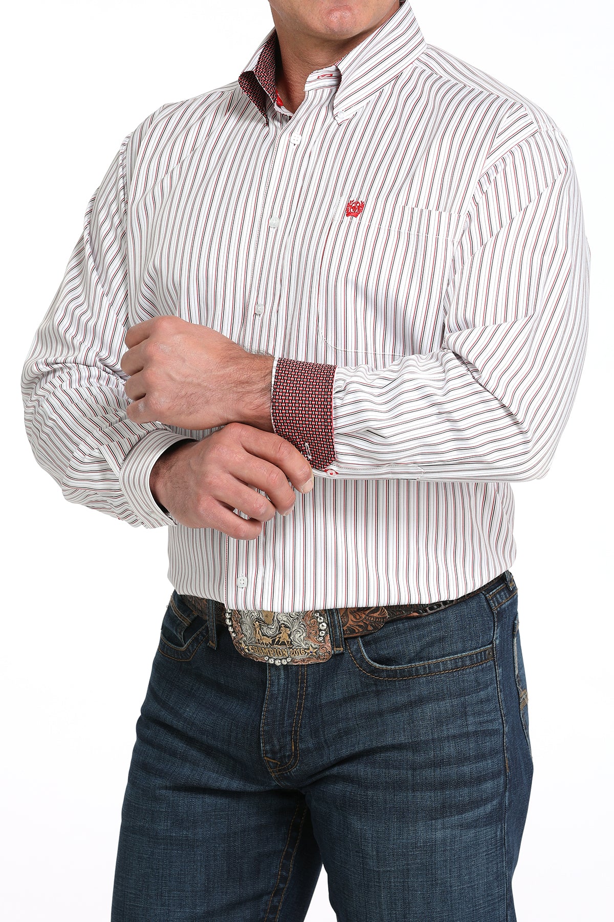 A man wearing a white striped button-up shirt with contrasting cuffs, dark jeans, and a large belt buckle, standing against a white background