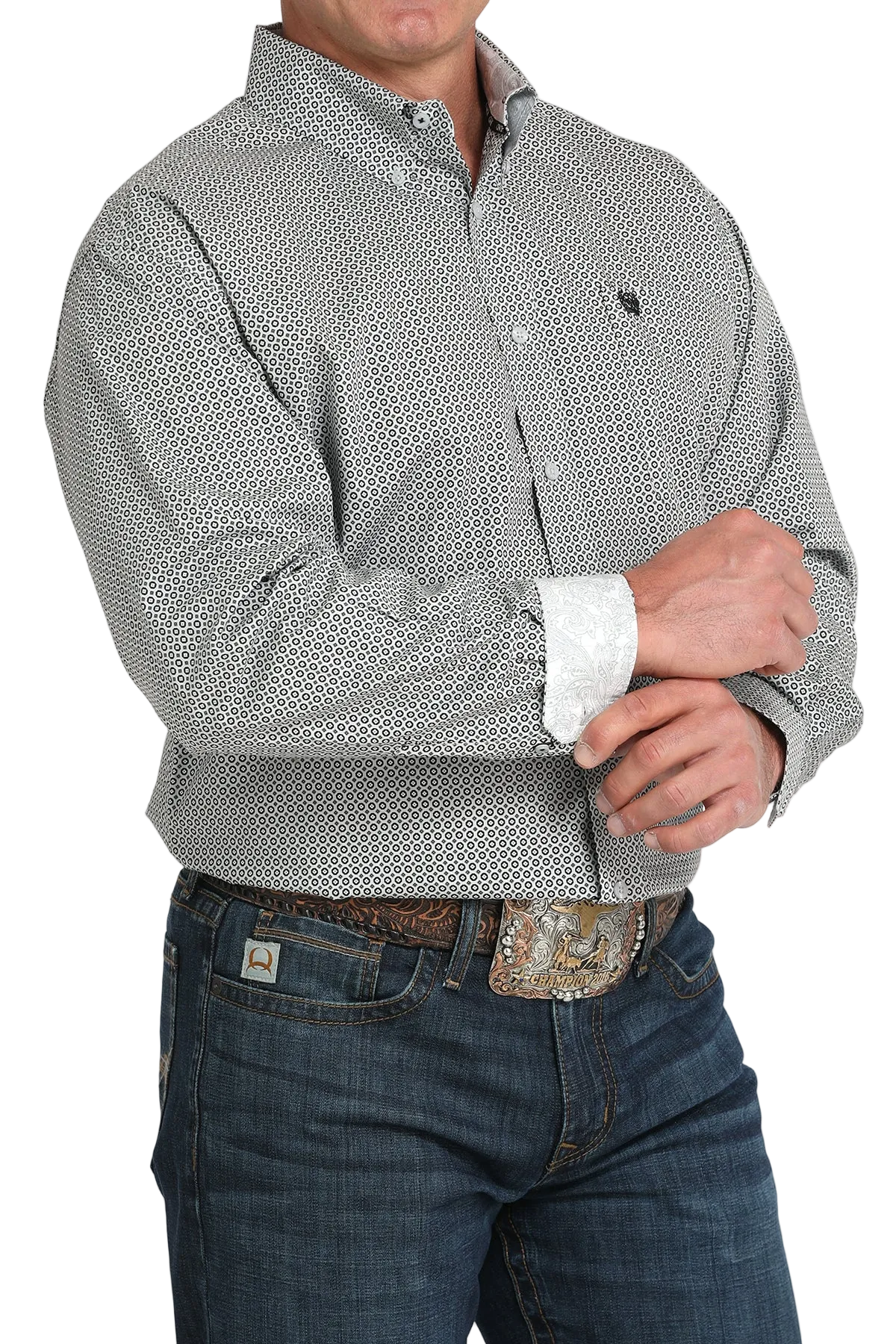 A man wearing a gray patterned button-up shirt with contrasting cuffs, dark jeans, and a large belt buckle, standing against a transparent background