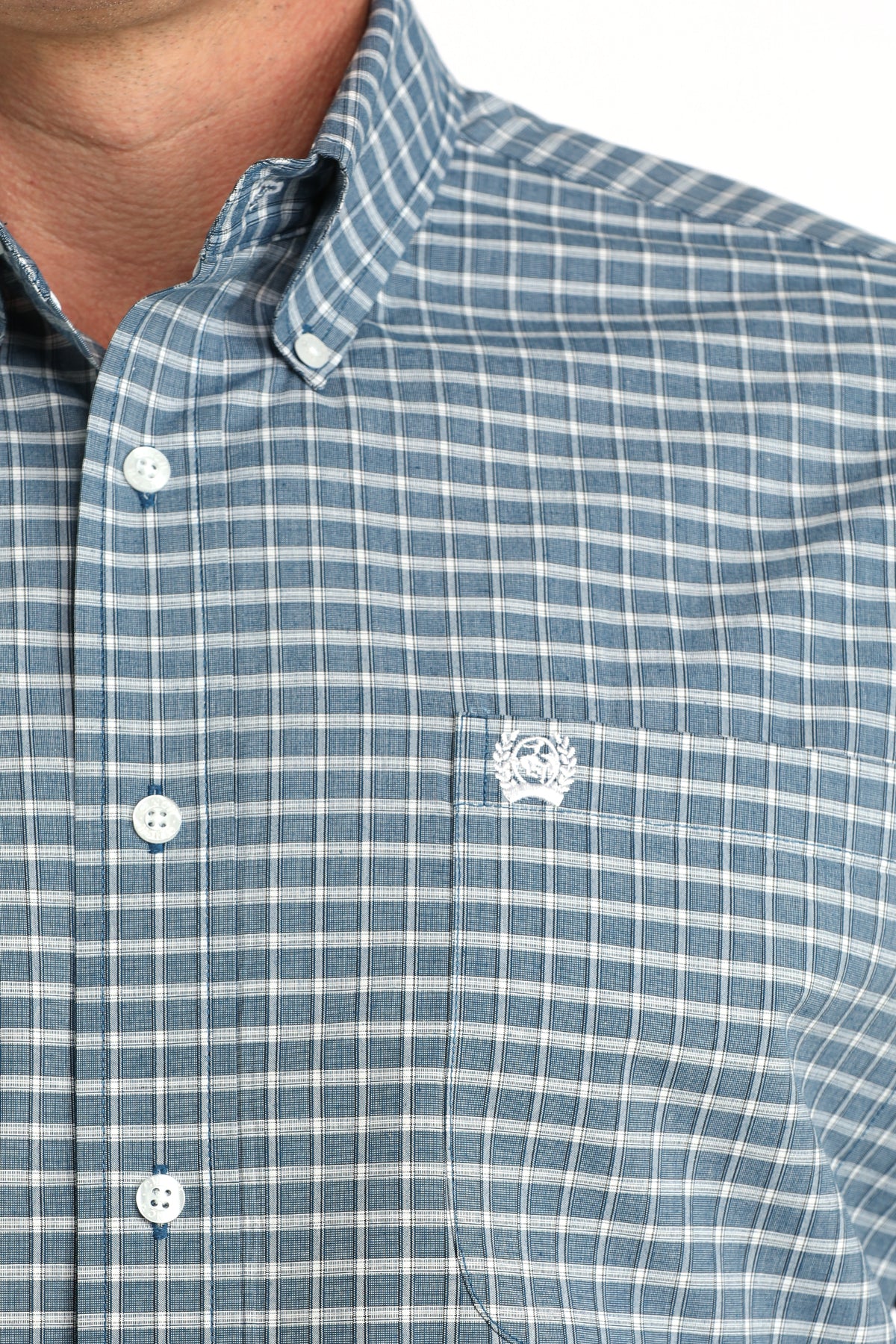 Close-up of a blue checkered shirt with a logo on the chest.