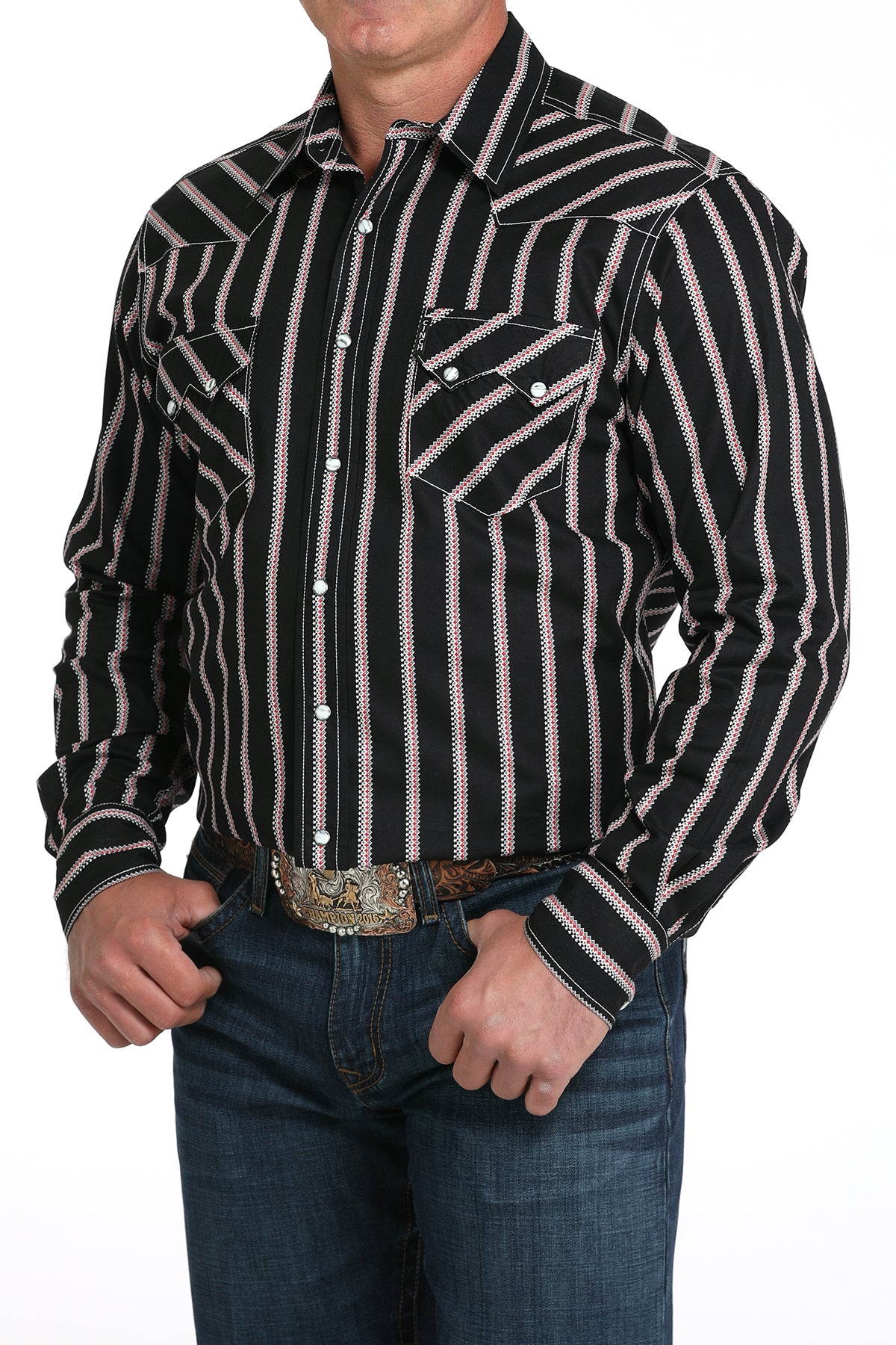 A man wearing a black striped button-up shirt, dark jeans, and a large belt buckle, standing against a white background