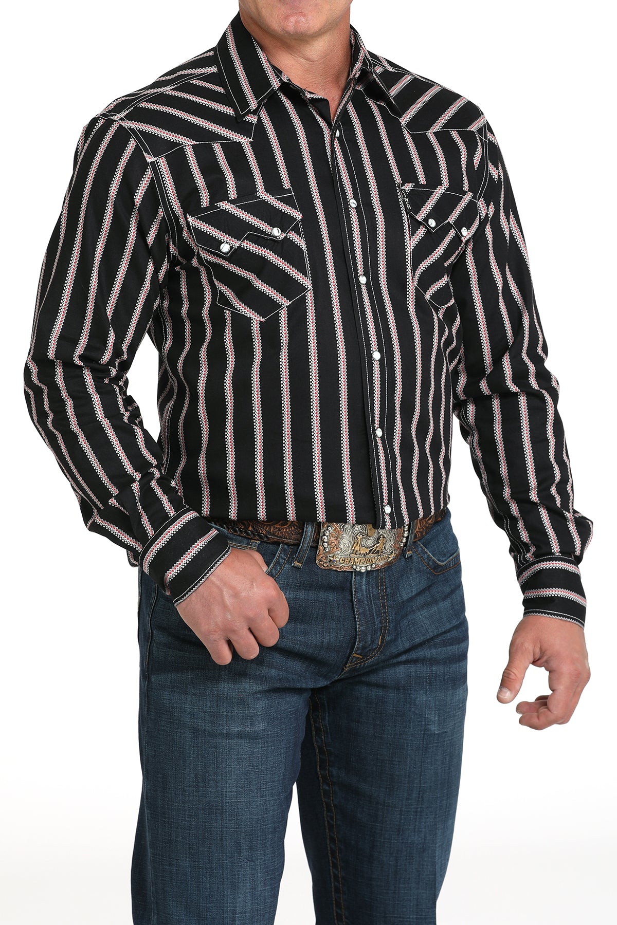 A man wearing a black striped button-up shirt, dark jeans, and a large belt buckle, standing against a white background