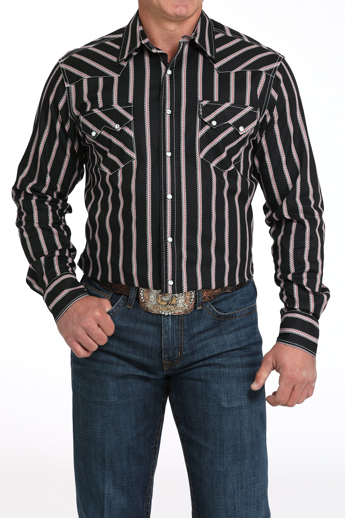 A man wearing a black striped button-up shirt, dark jeans, and a large belt buckle, standing against a white background