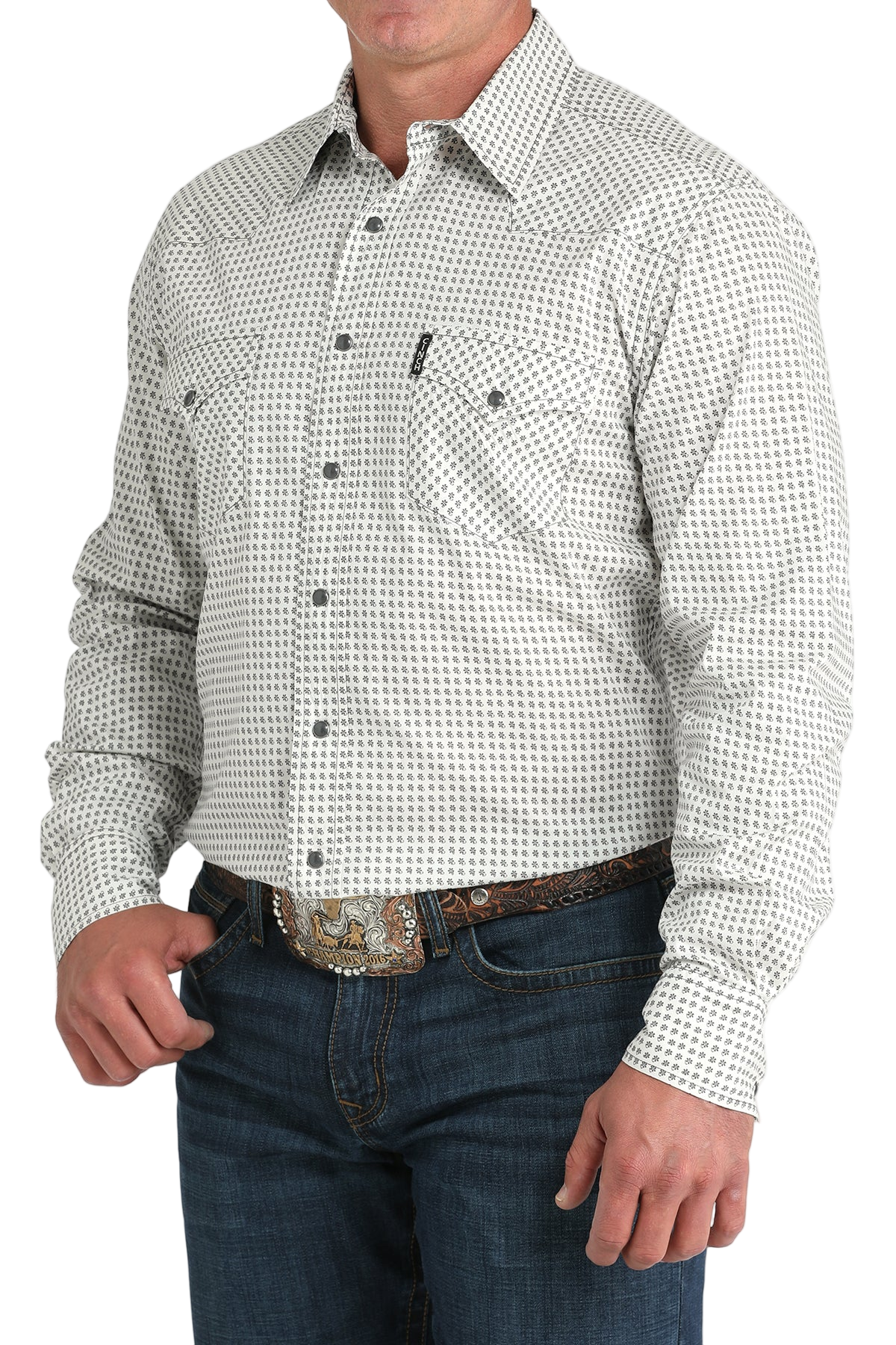 Man wearing a light gray patterned button-up shirt with blue jeans on a white background