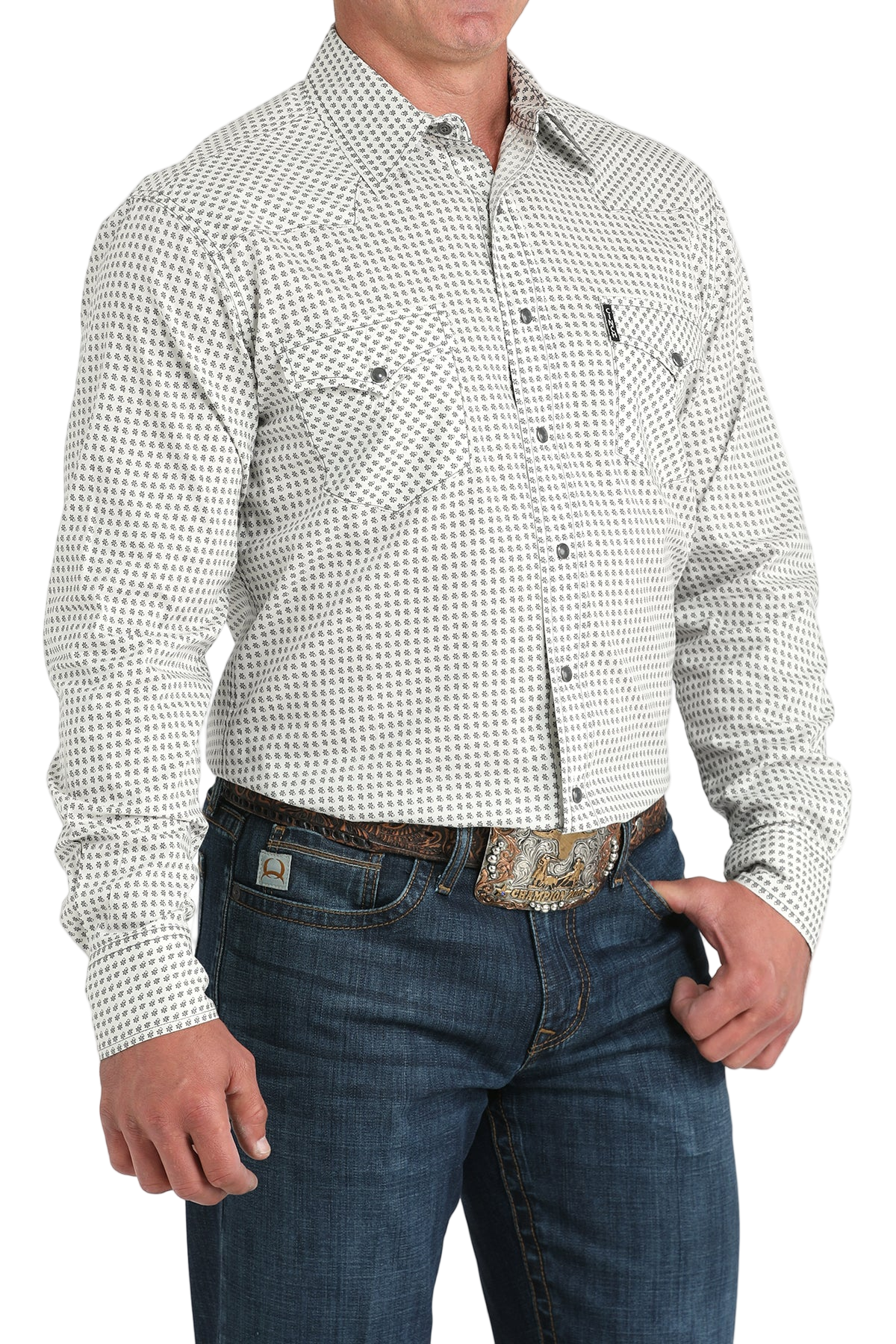 Man wearing a light gray patterned button-up shirt with blue jeans on a white background