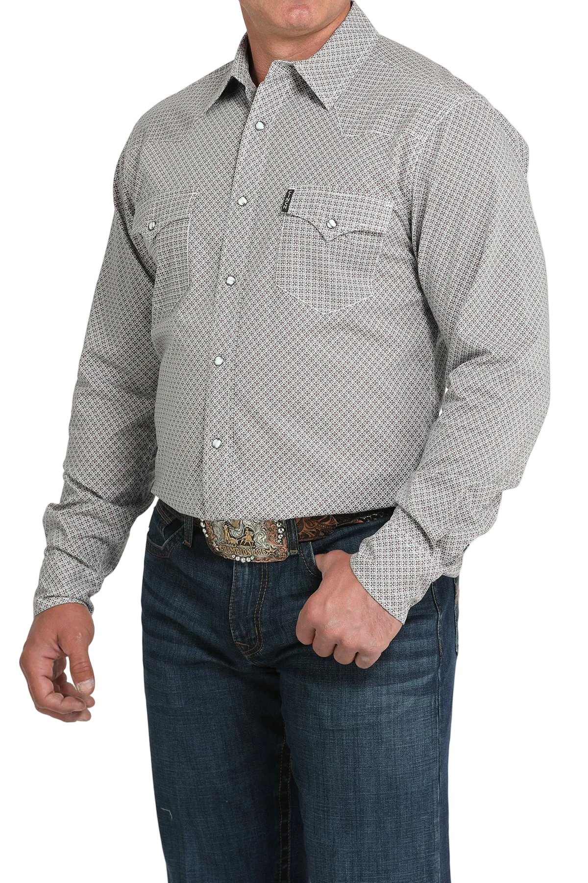 A man wearing a light gray patterned button-up shirt, dark jeans, and a large belt buckle, standing against a transparent background