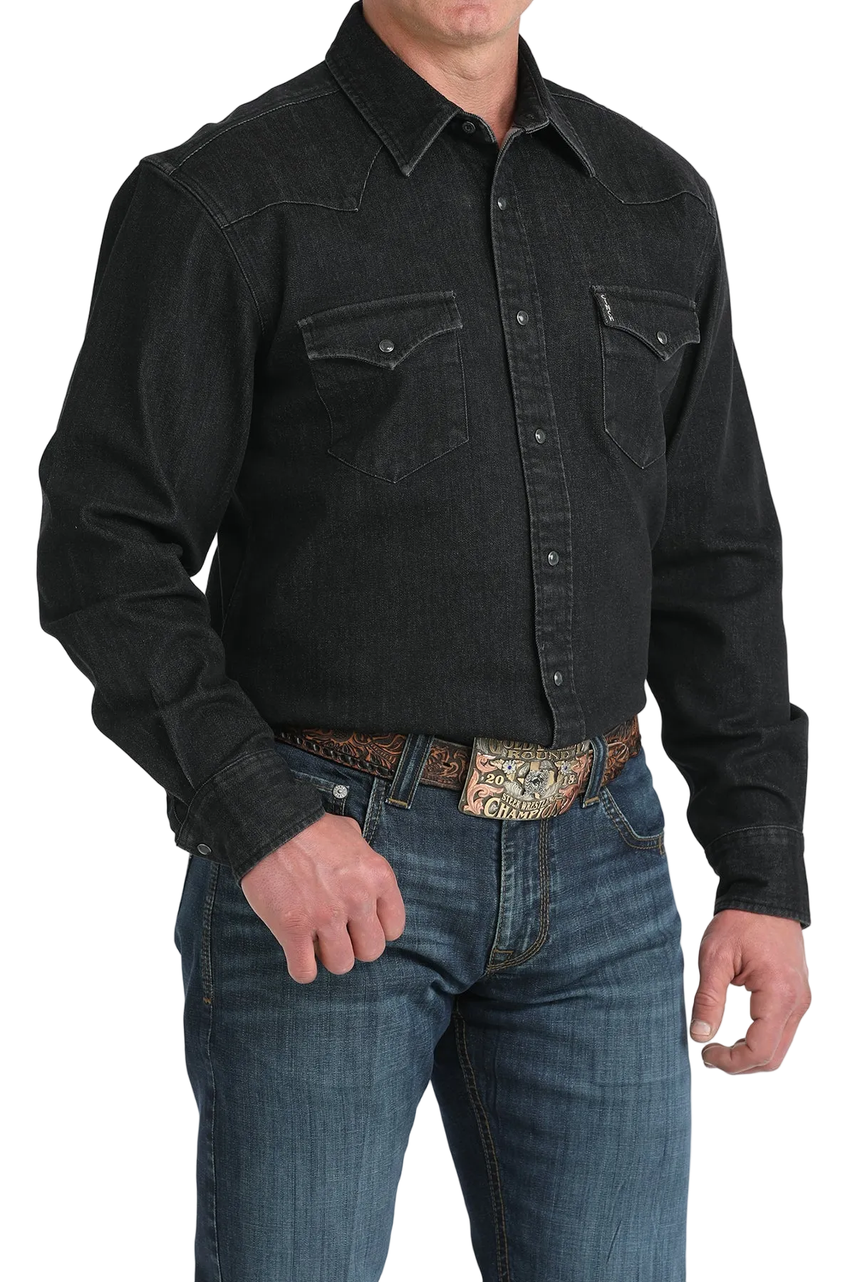 Man wearing a black denim shirt and blue jeans with a patterned belt.