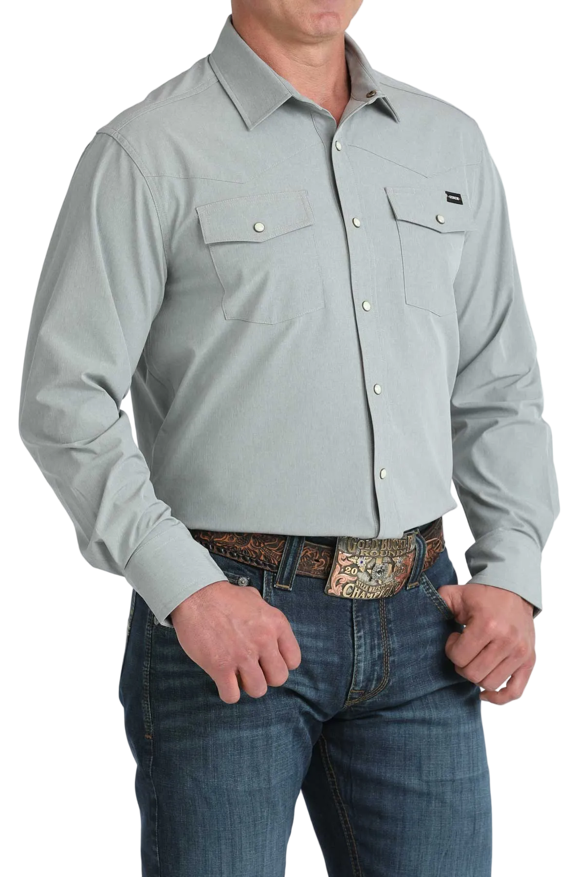 Man wearing a light gray button-up shirt and blue jeans with a patterned belt on a white background